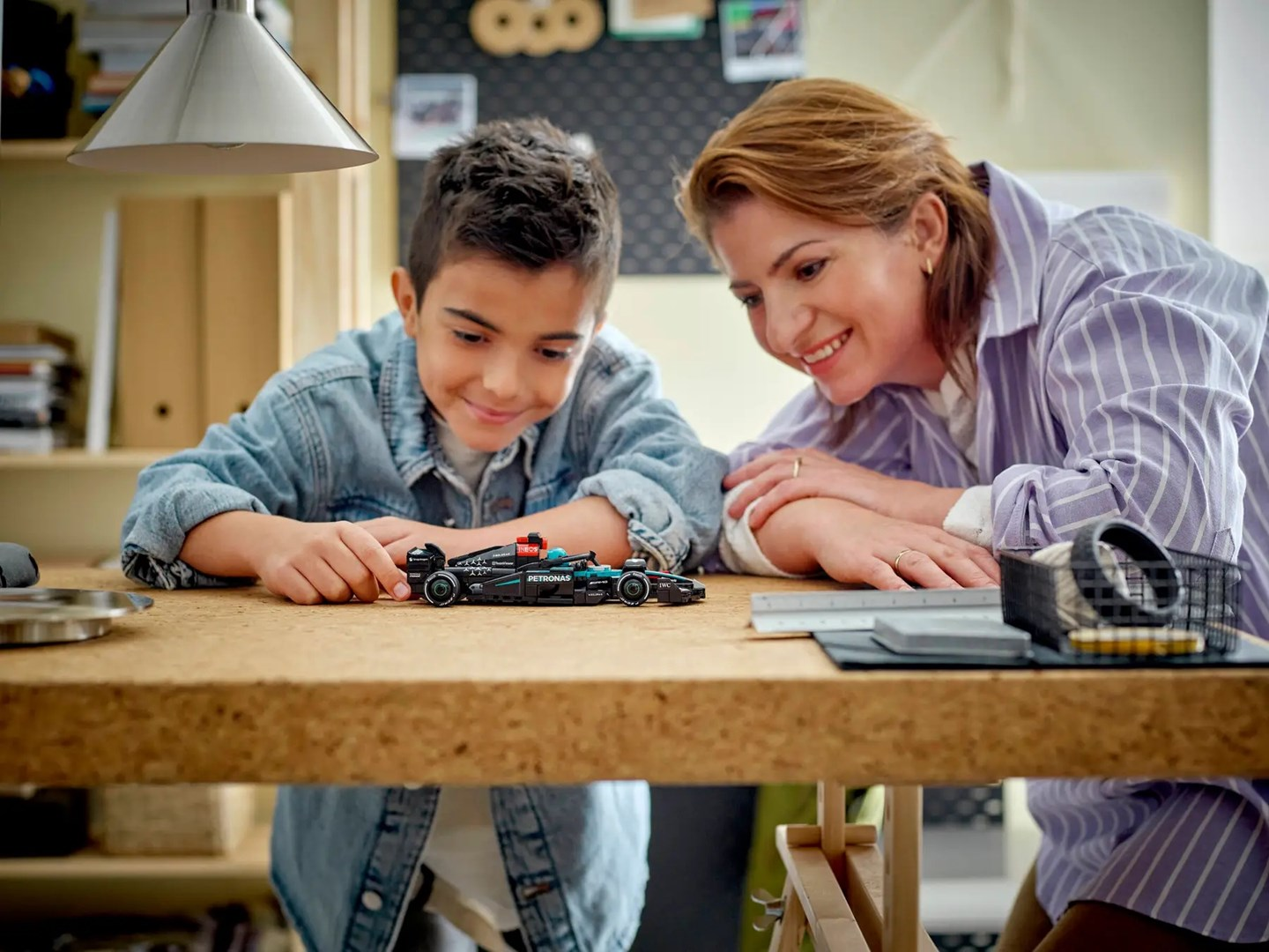 Chłopiec i kobieta patrzą i uśmiechają się do zabawkowego samochodu na drewnianym stole.