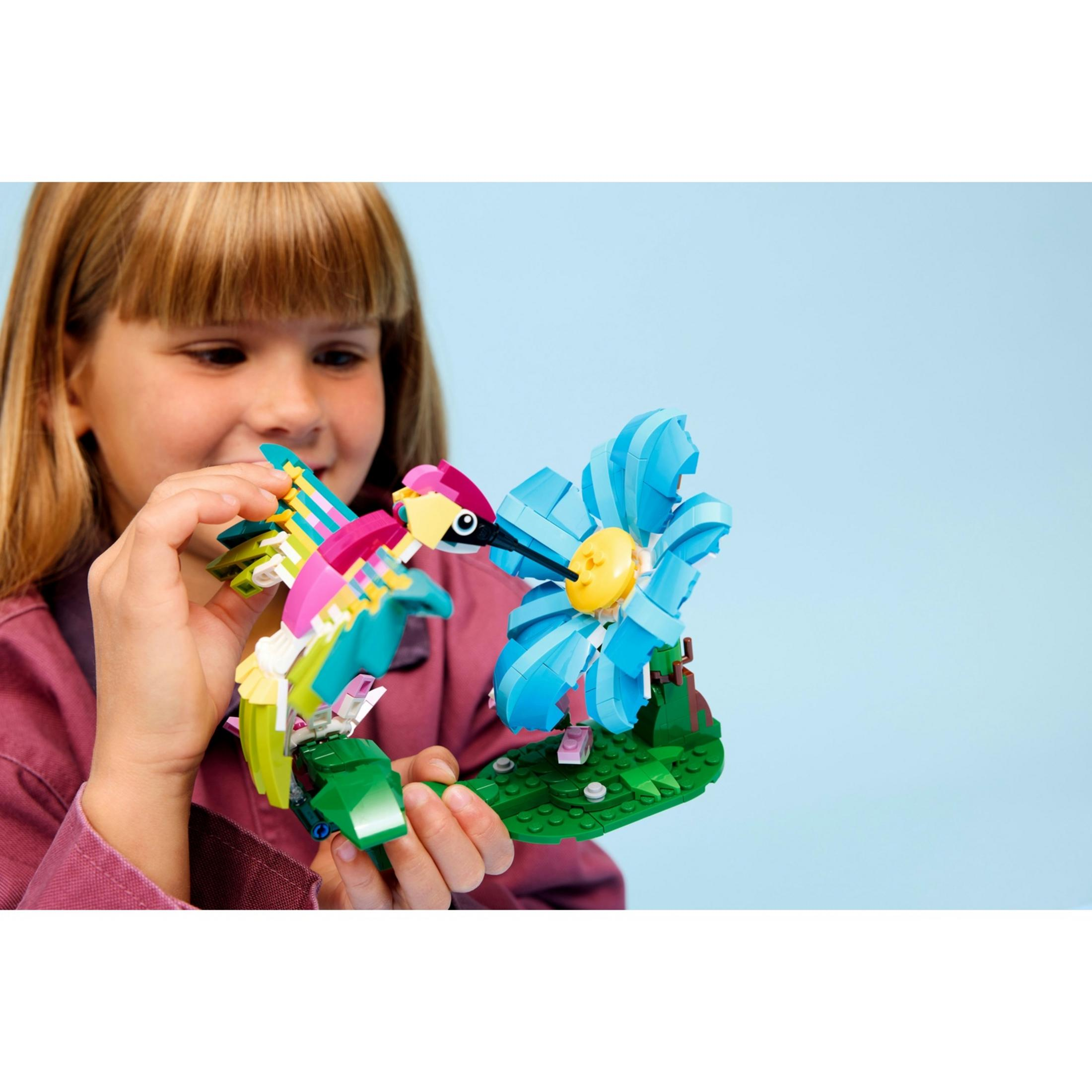 Dziecko trzyma kolorowego Lego kolibra na tle niebieskiego.