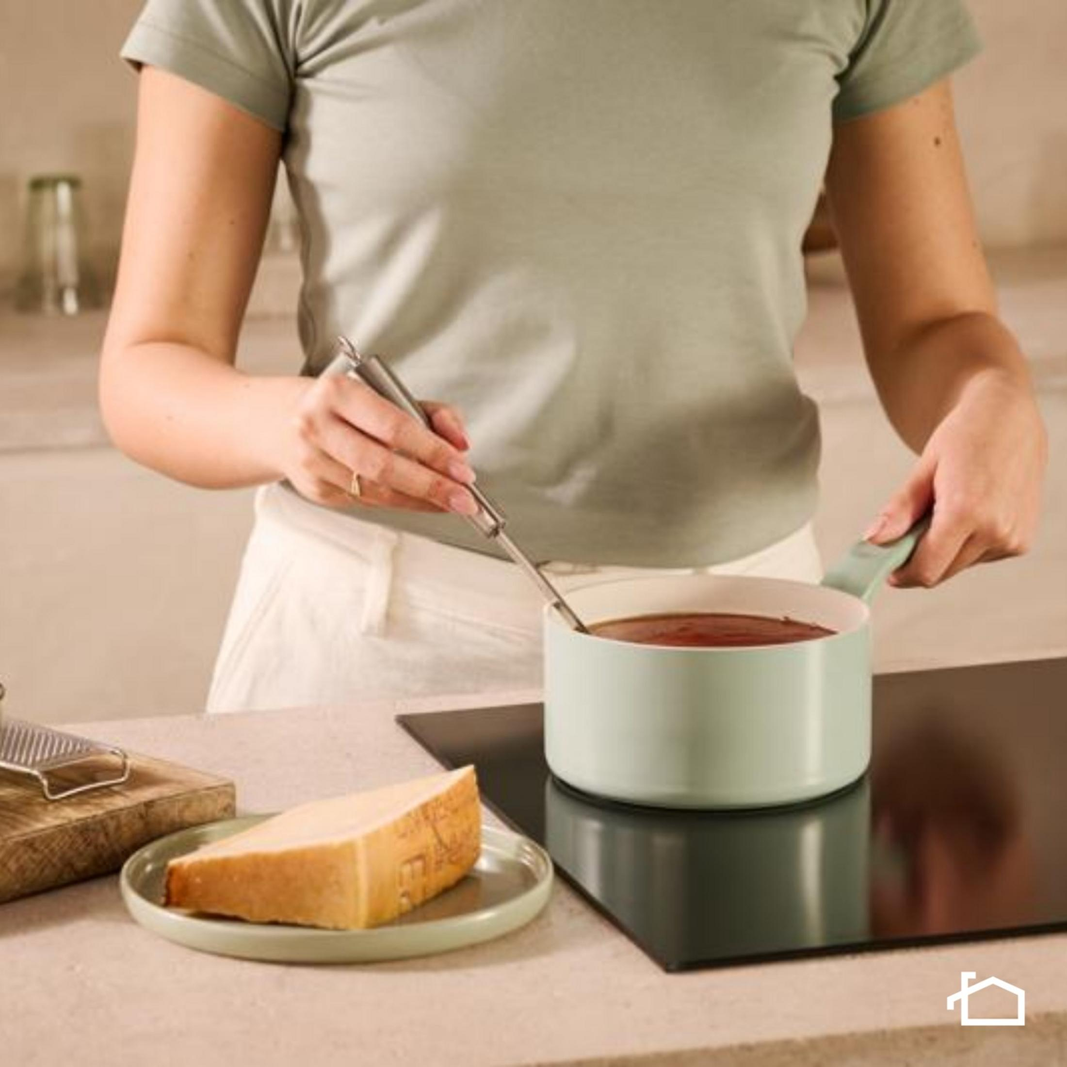 Persona cocinando con una olla en una estufa. Queso y rallador cerca.