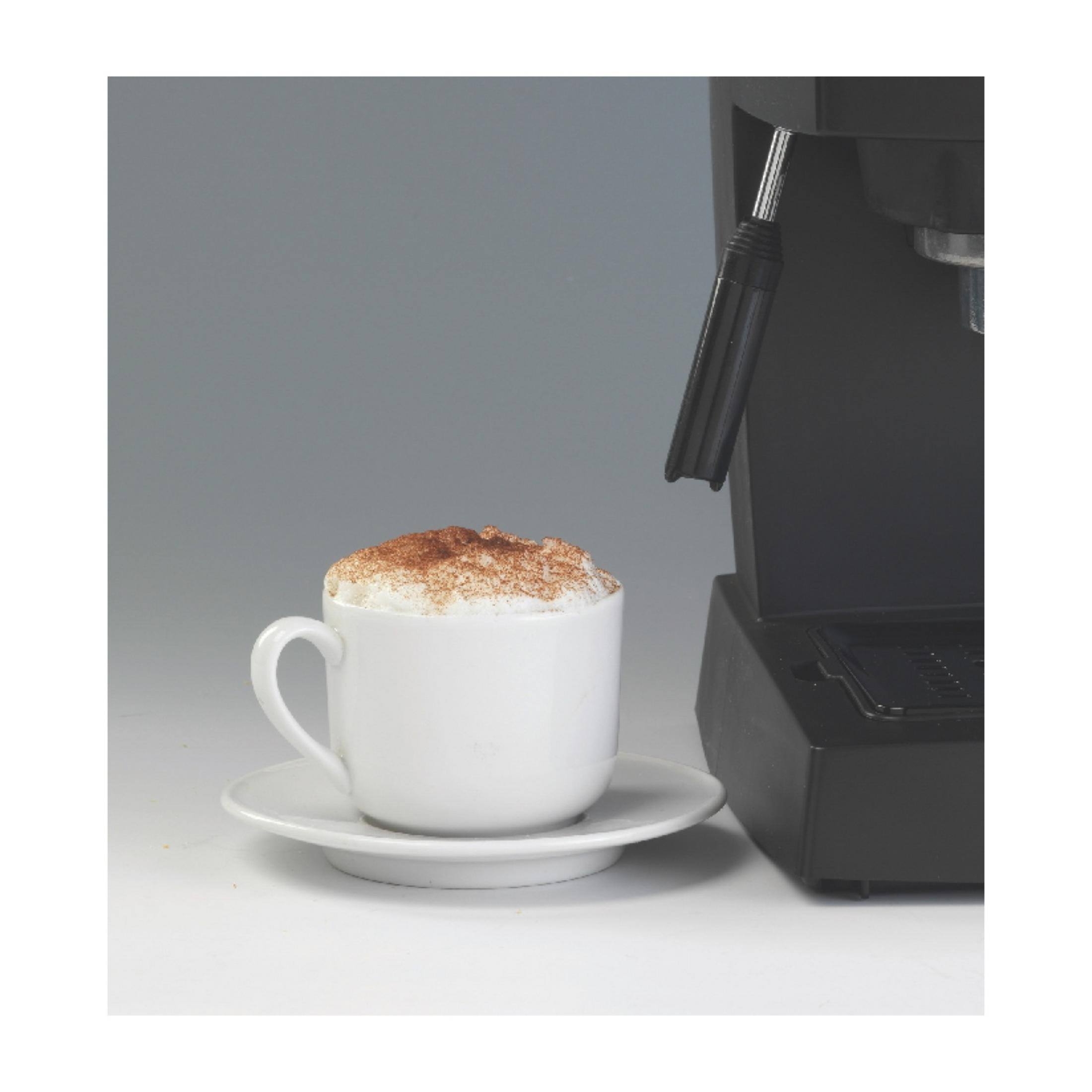 Biała filiżanka cappuccino z cynamonem obok ekspresu do kawy.