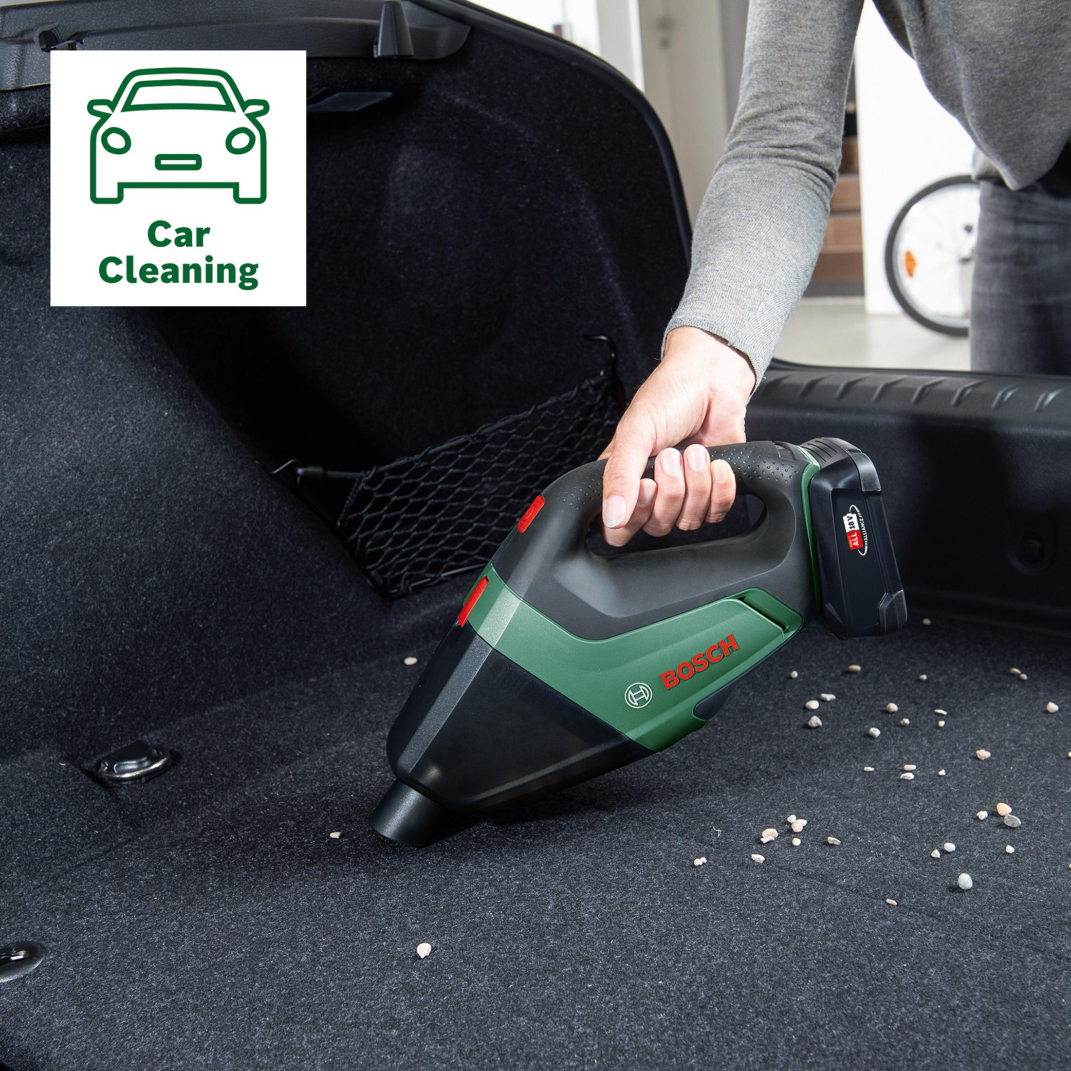 Bir el, bir arabanın bagajında yeşil bir Bosch akülü süpürge tutuyor.