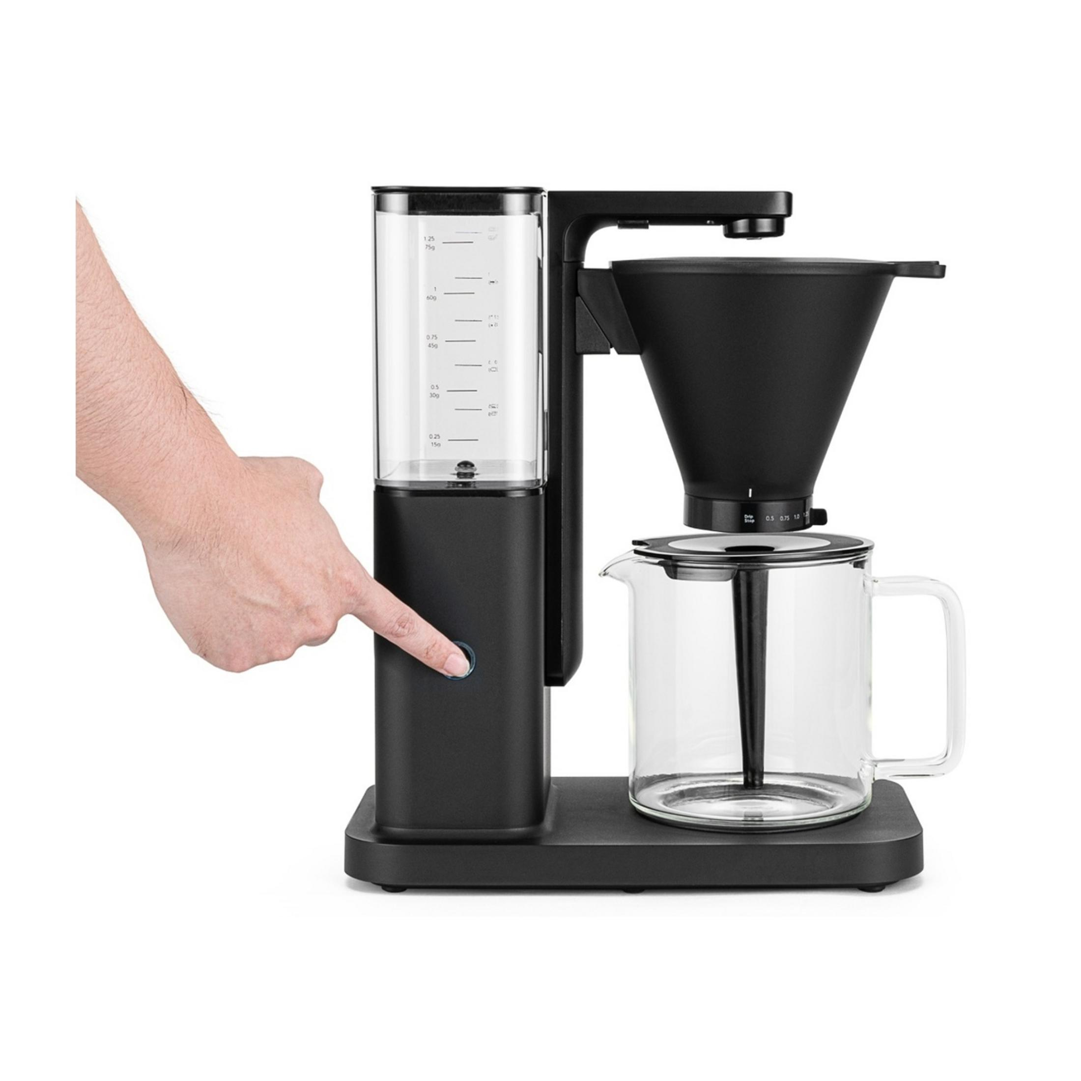 Una mano preme un pulsante su una macchina da caffè nera con caraffa di vetro.