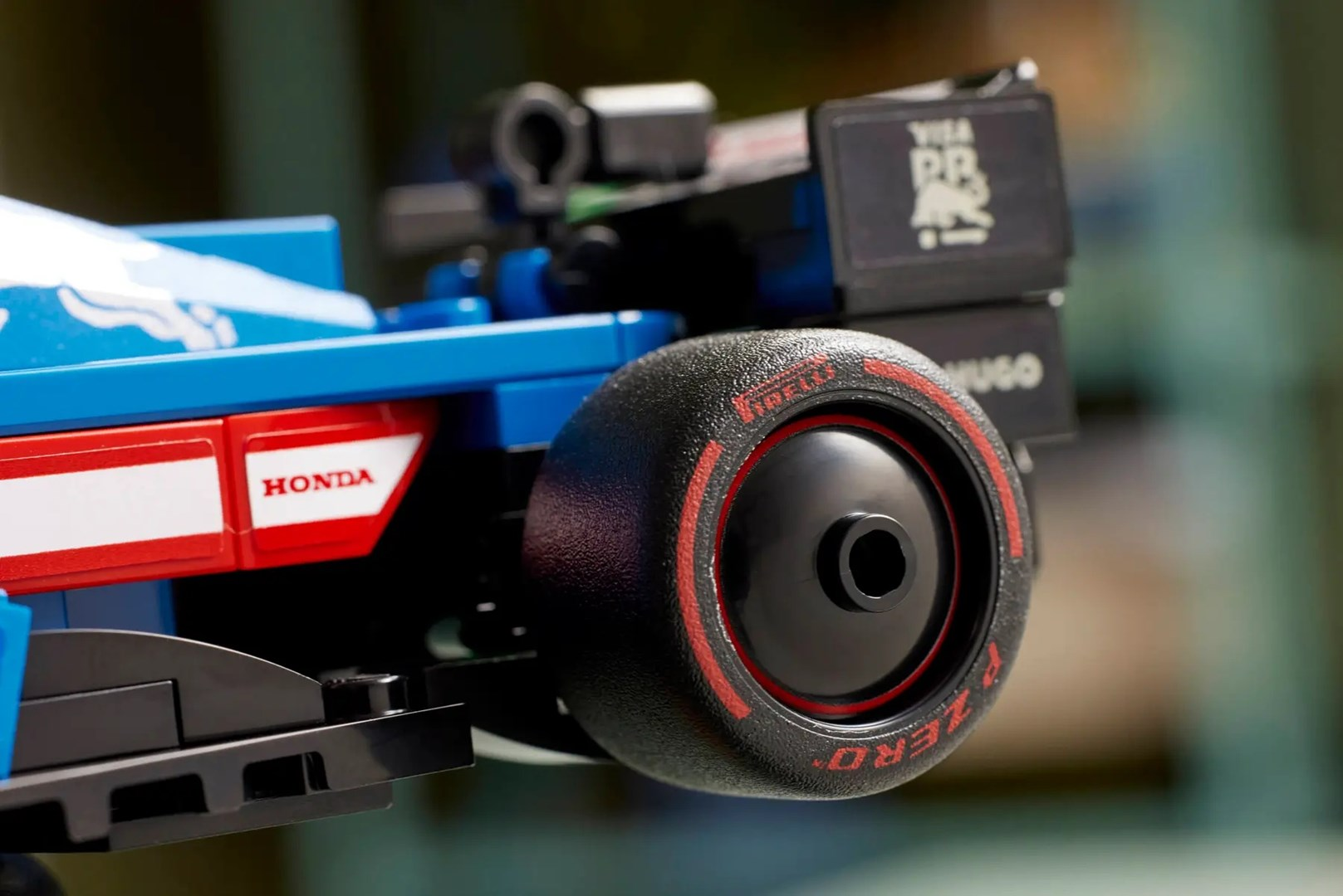 Niebieski samochód wyścigowy z logo HONDA i czerwonymi akcentami na kole.