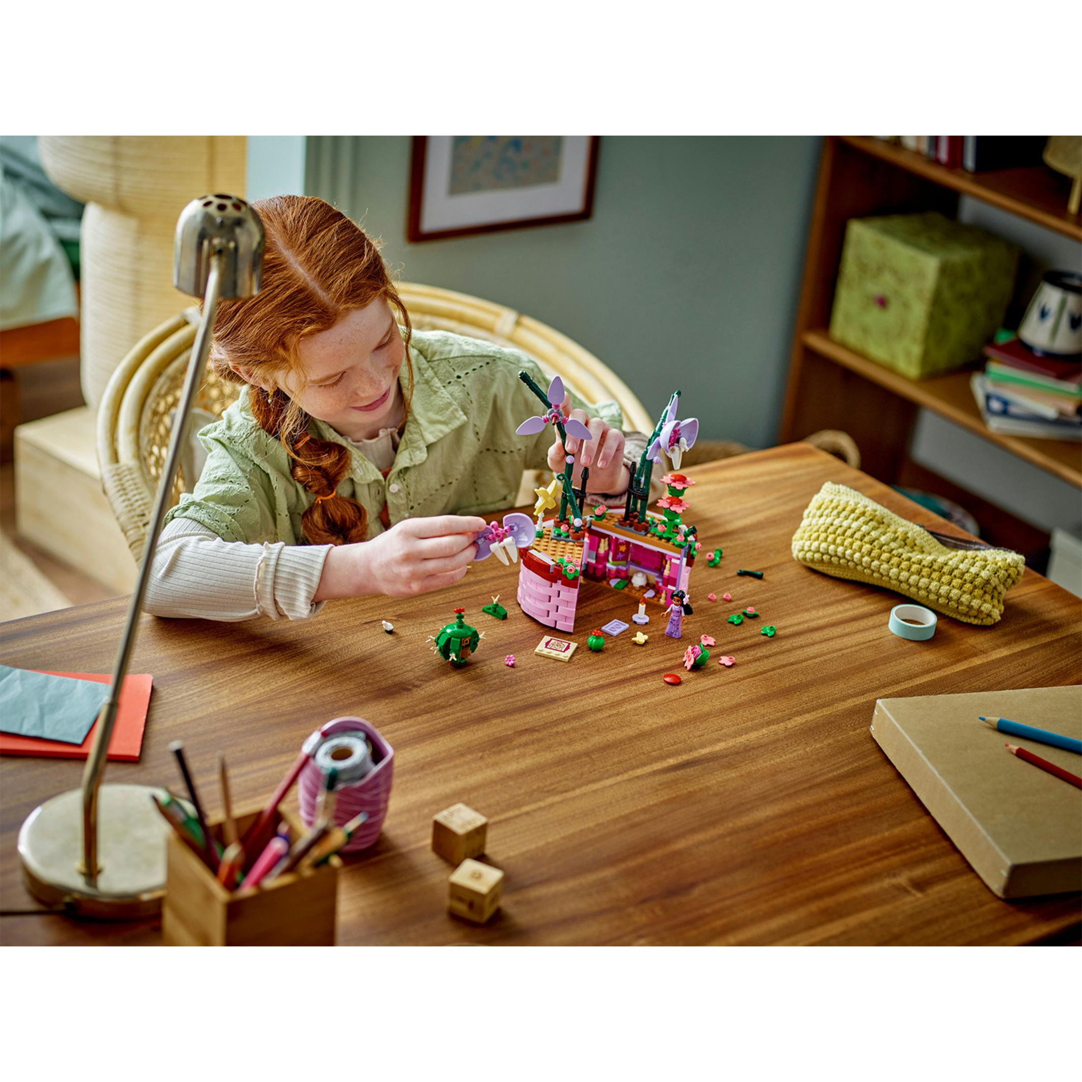 Una niña pelirroja construye un modelo de Lego en una mesa de madera.