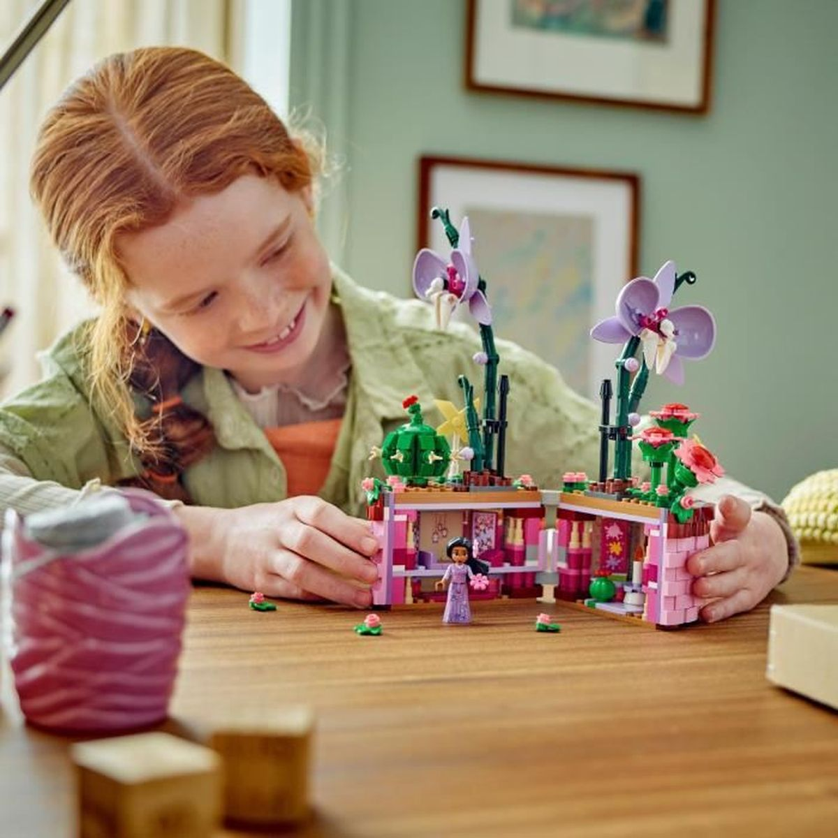 Una niña construye una casa de flores de Lego con orquídeas moradas y una figura.
