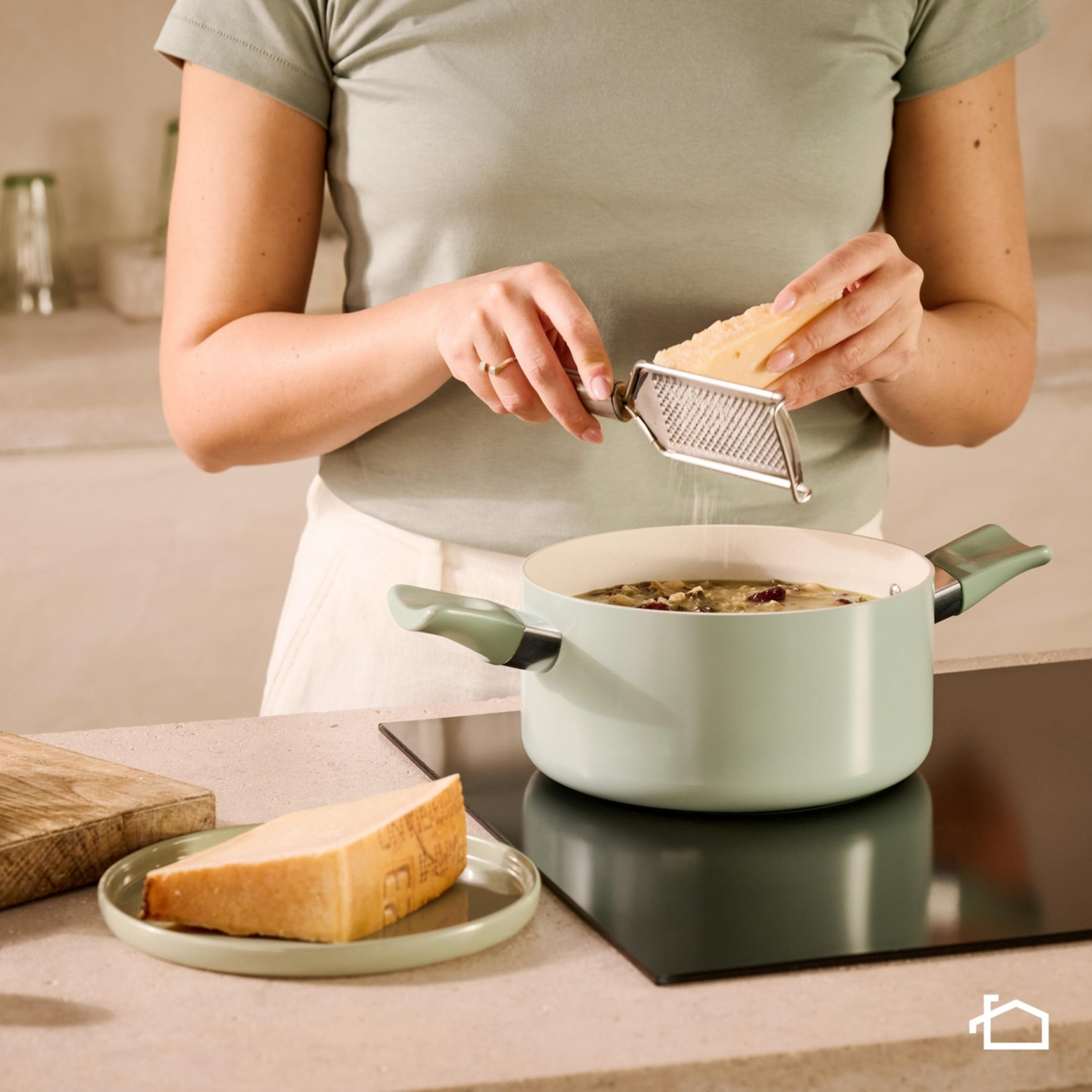 Una persona ralla queso sobre una olla de comida.