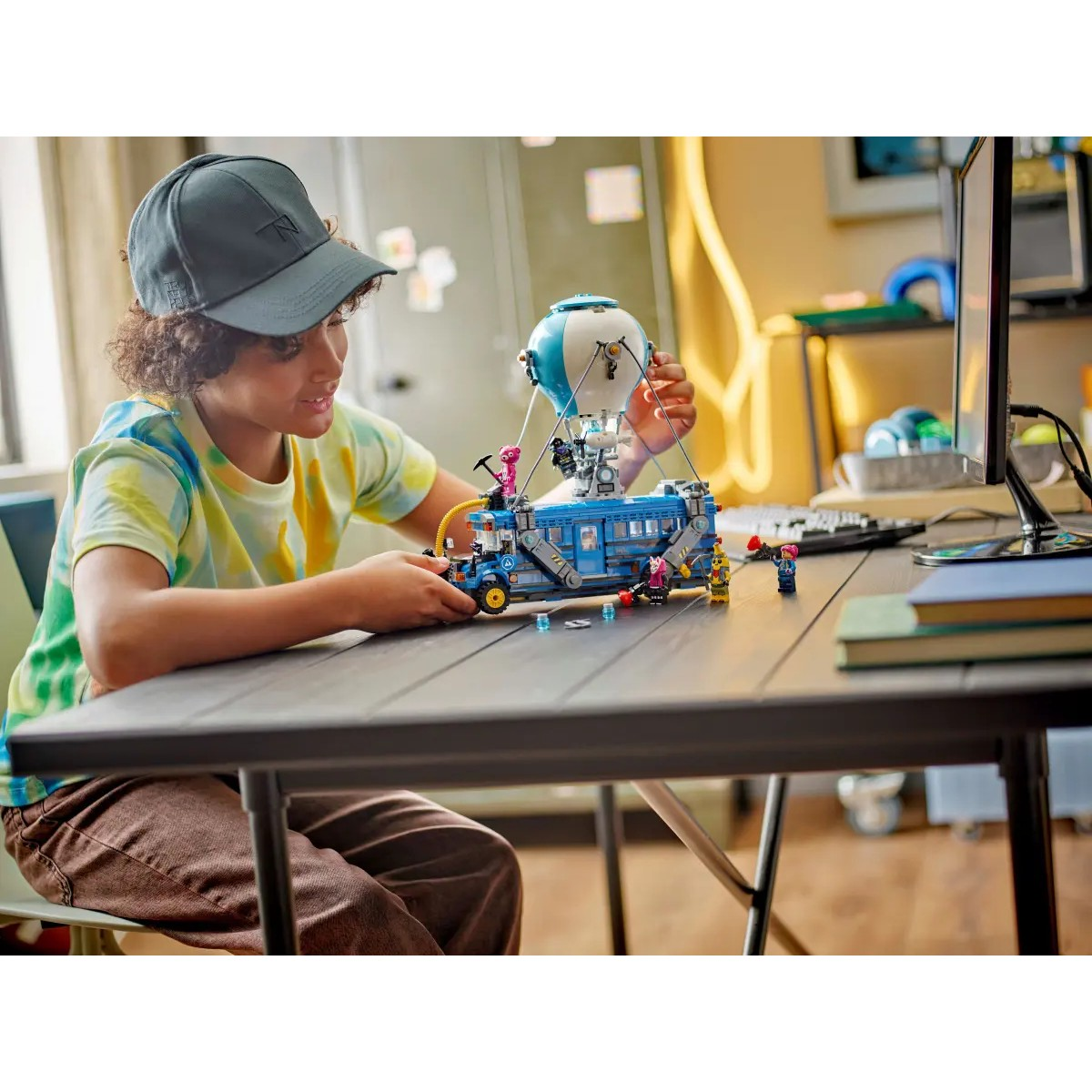 Chłopiec bawi się niebieskim autobusem Lego z balonem i figurkami przy stole.