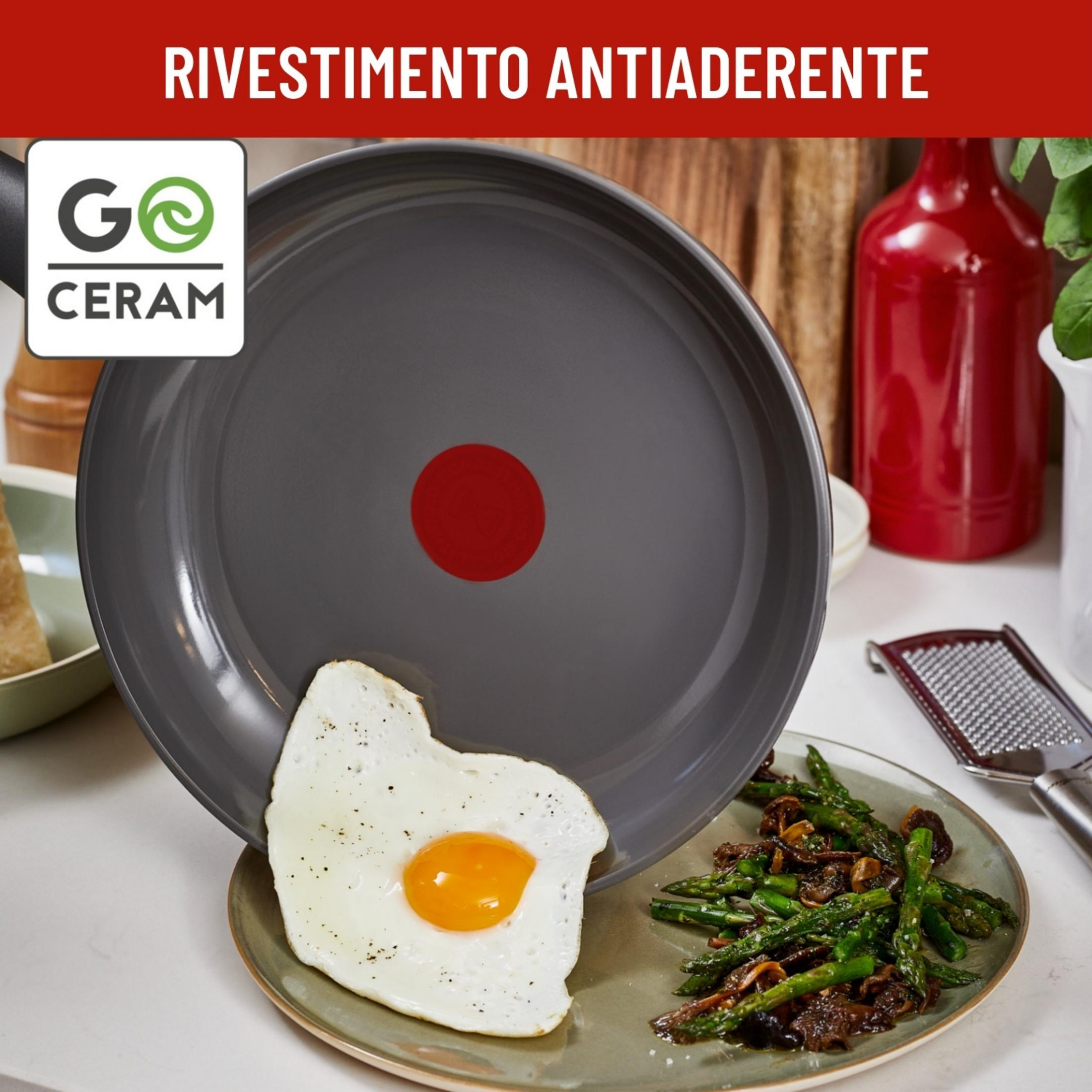 Sartén gris con punto rojo, al lado un huevo frito y espárragos con champiñones.