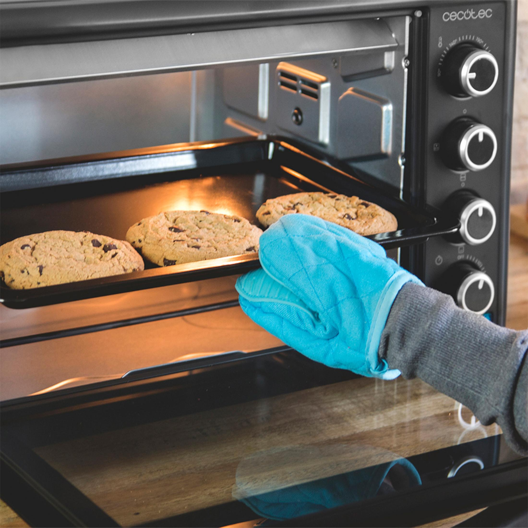 Ręka w niebieskiej rękawicy kuchennej wyjmuje ciasteczka z piekarnika.