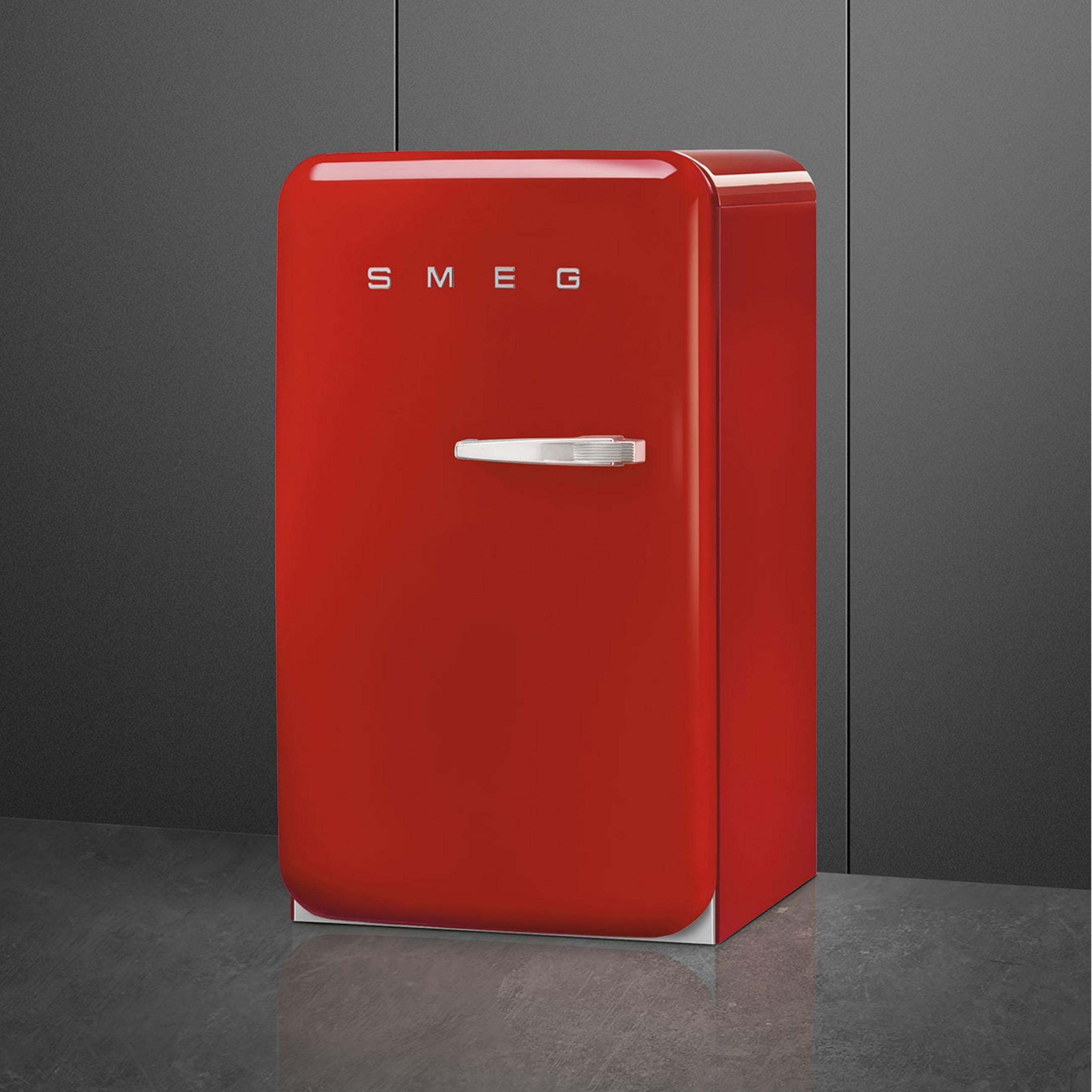 Un pequeño frigorífico Smeg rojo con asa plateada sobre suelo oscuro.