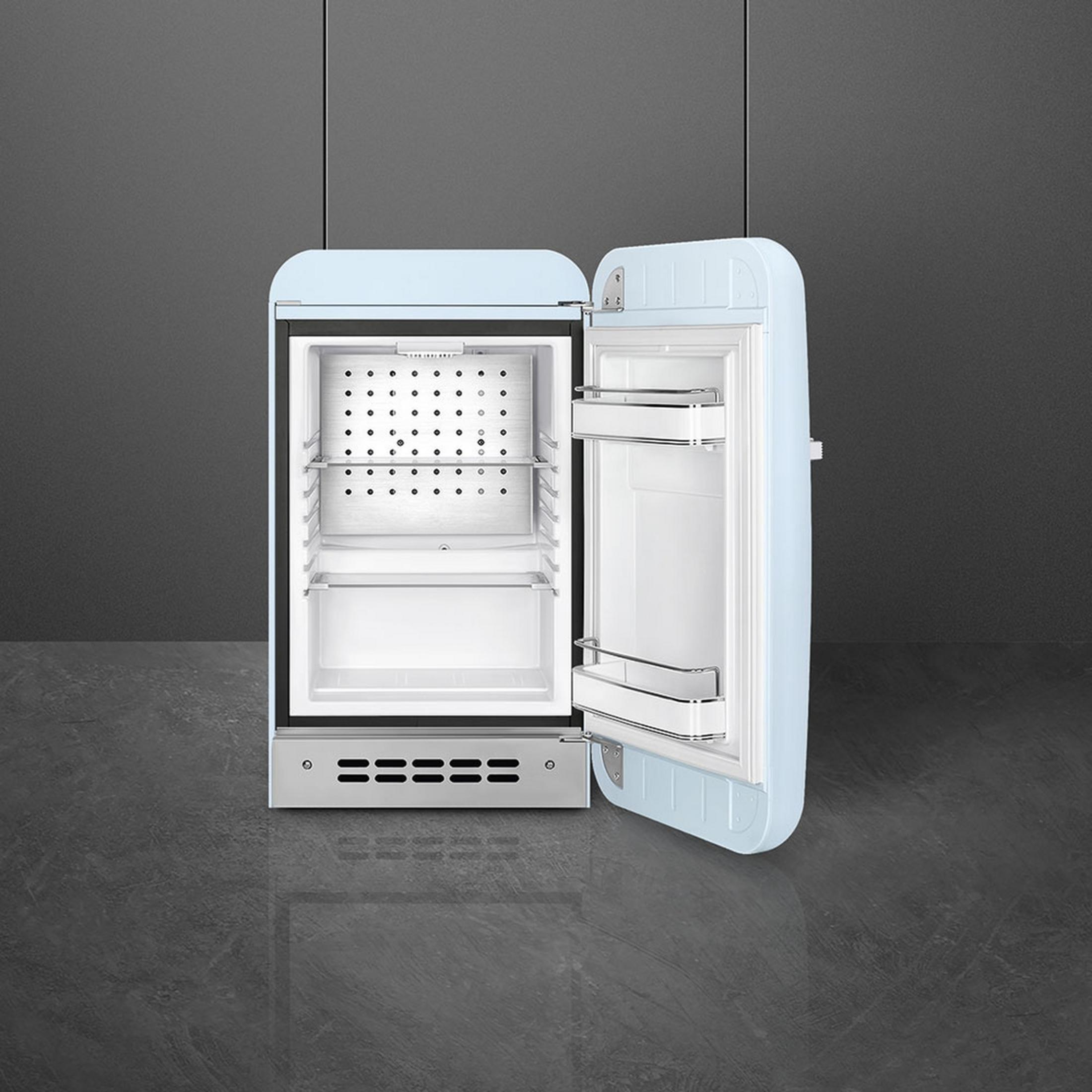 Un refrigerador retro azul claro con la puerta abierta. Interior blanco con estantes.