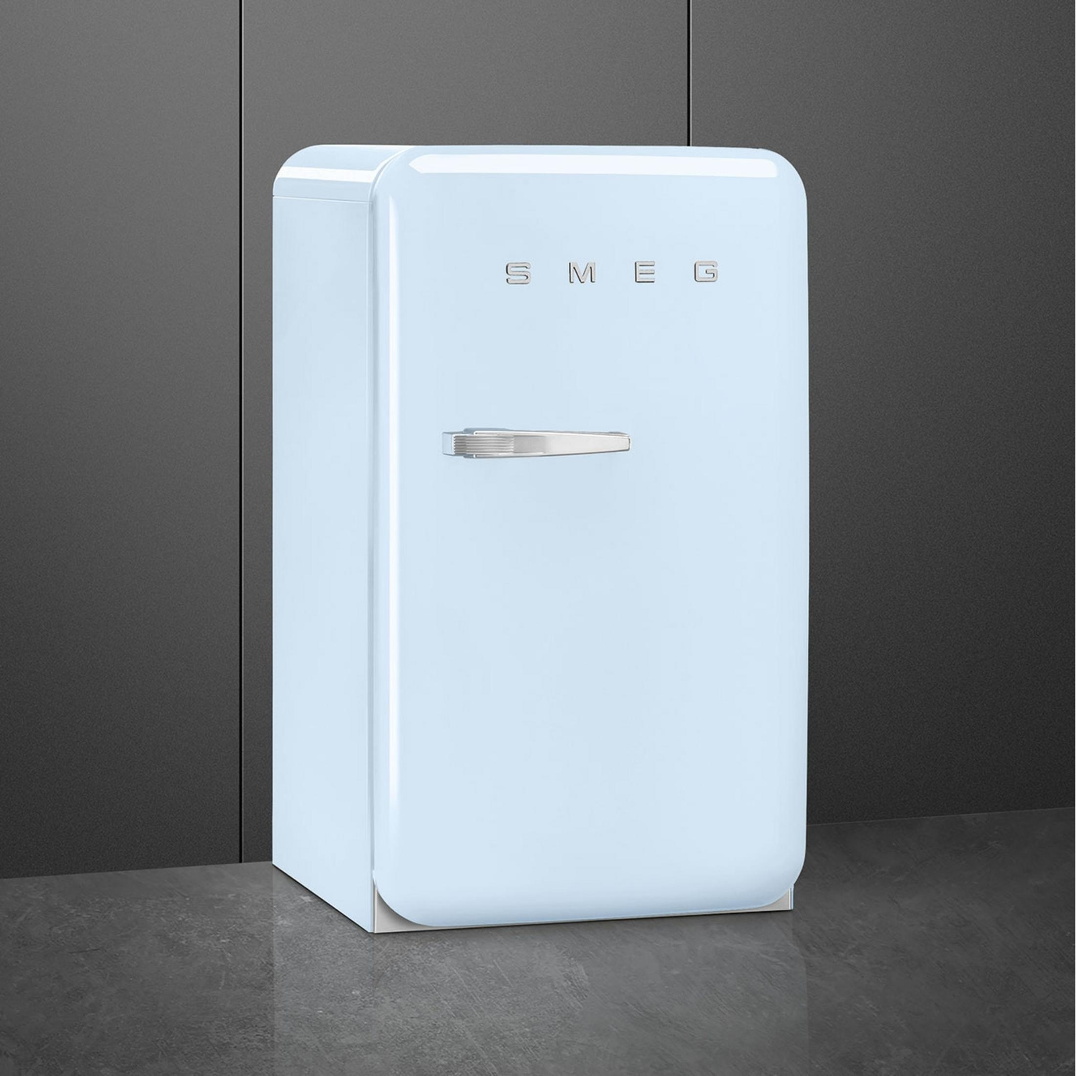 Un refrigerador Smeg azul claro con asa plateada sobre suelo oscuro.