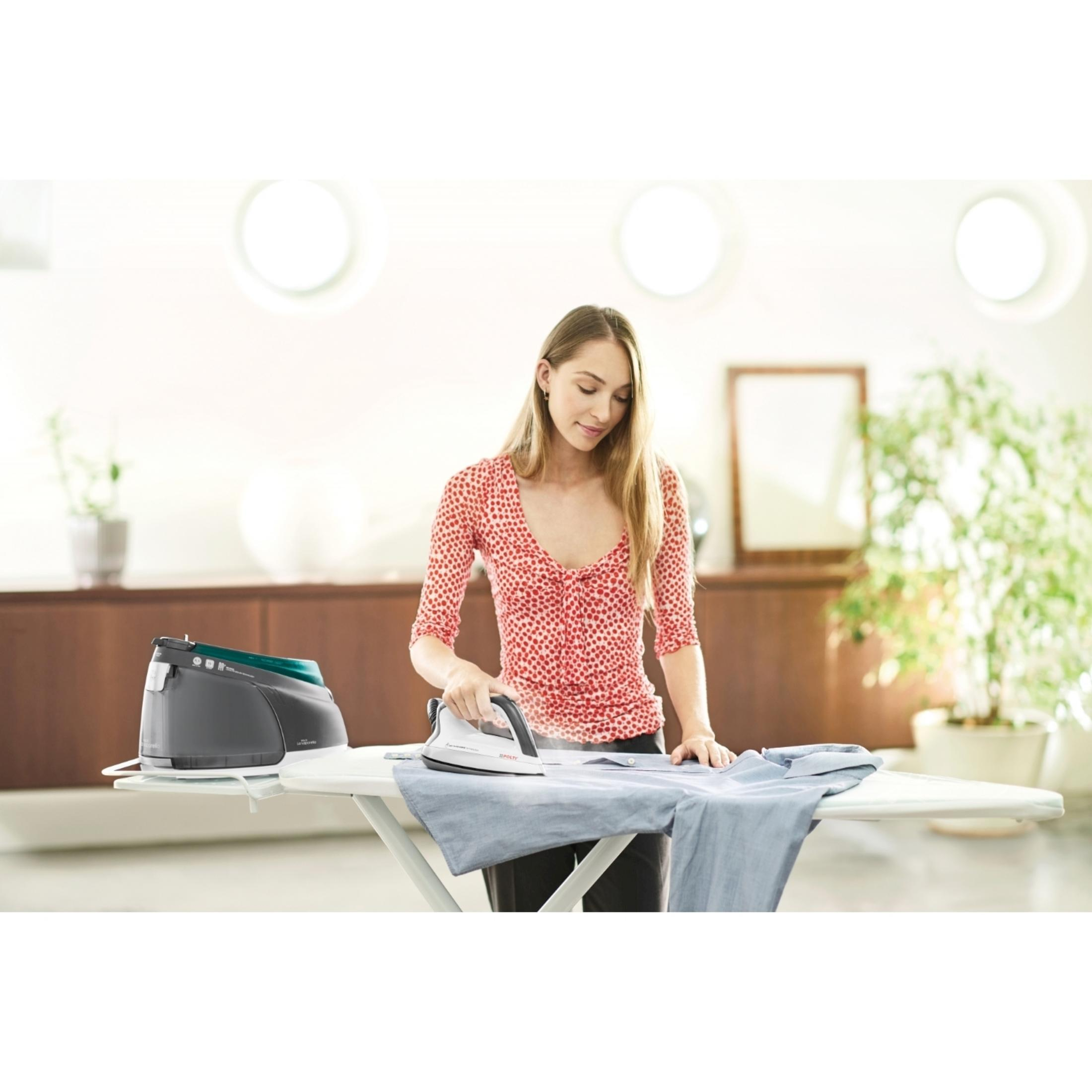Una mujer plancha una camisa azul en una tabla de planchar con una plancha de vapor.