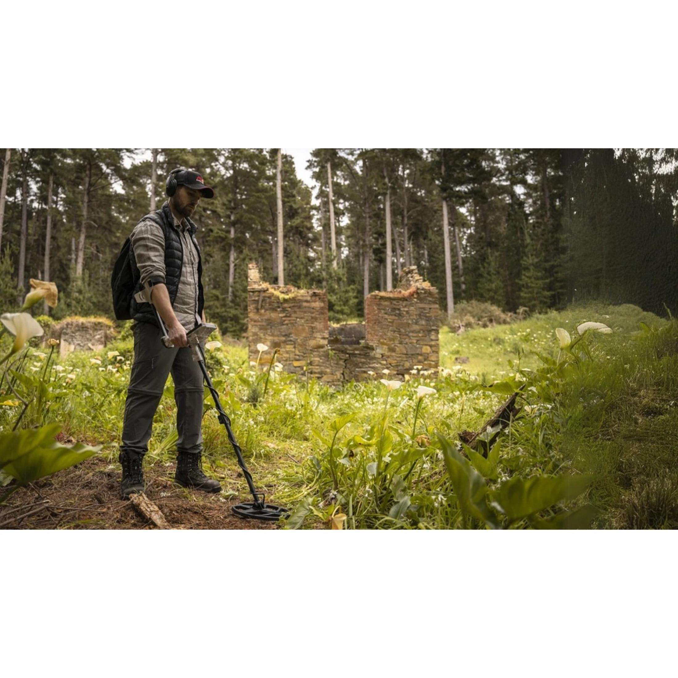Ein Mann mit Kopfhörern und Rucksack sucht mit einem Metalldetektor in der Nähe einer Ruine.
