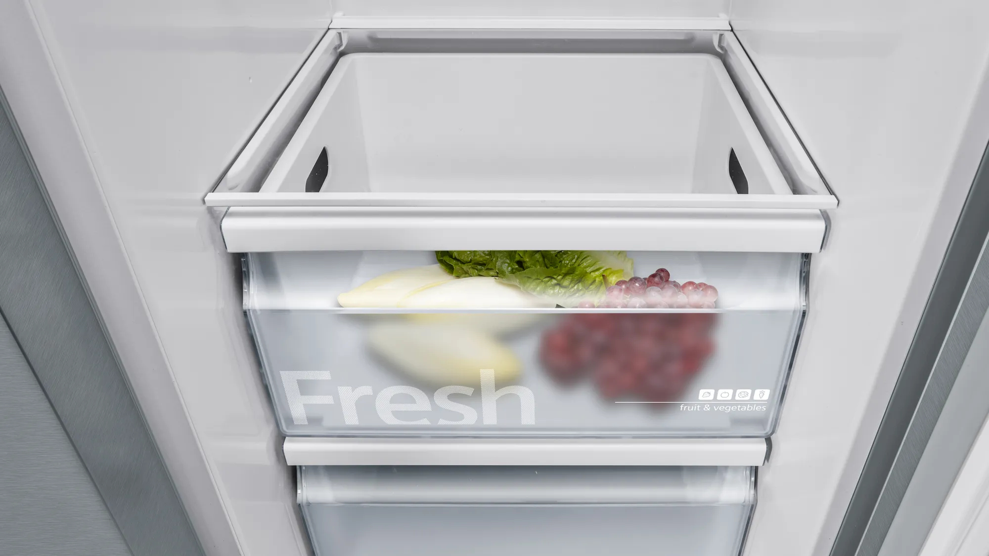 Ein Kühlschrankfach mit Salat, Endivien und roten Trauben. Das Wort „Fresh“ ist sichtbar.
