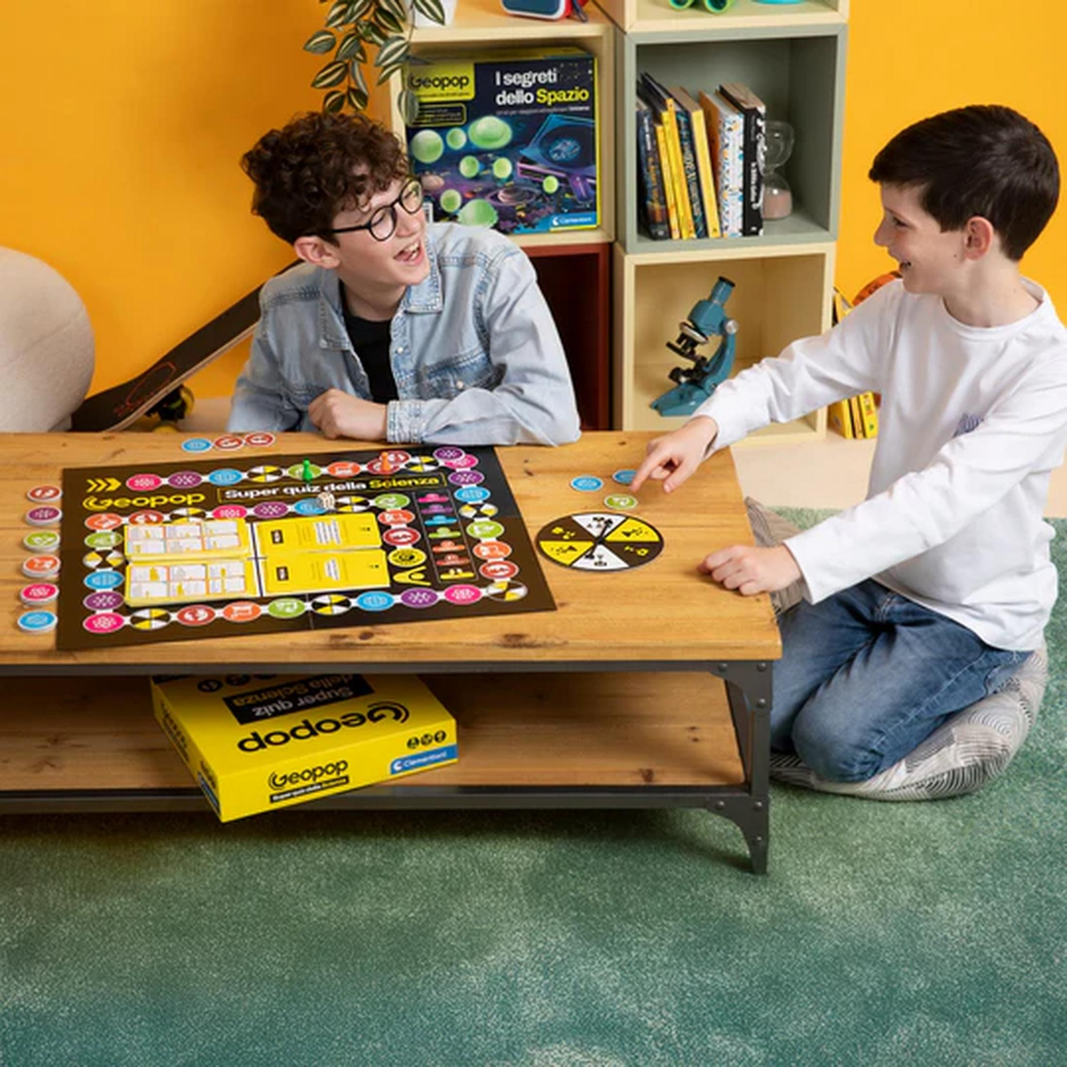 Due ragazzi giocano a un gioco da tavolo su un tavolo di legno, con libri e un microscopio sullo sfondo.