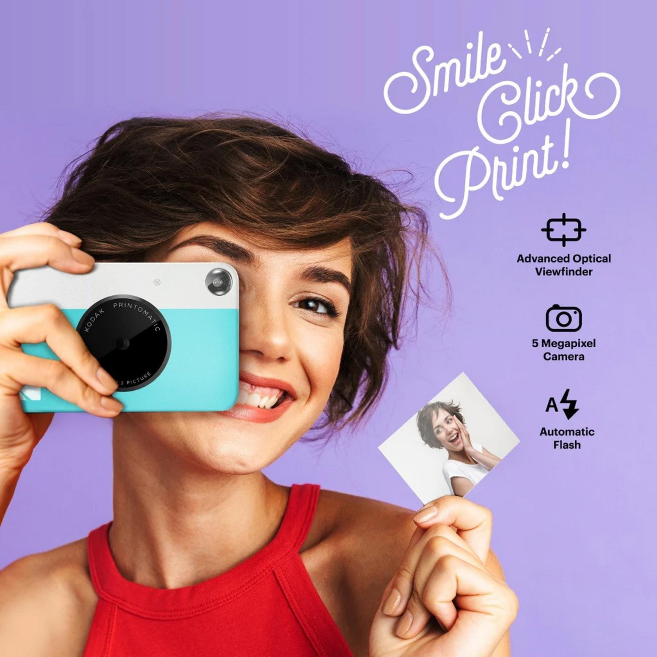 Une femme tient un appareil photo turquoise devant son visage et sourit.