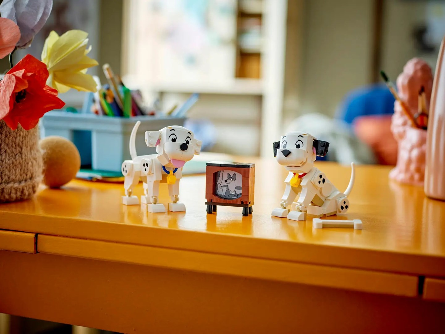 Turuncu bir masada iki Lego dalmaçyalı yavrusu ve bir televizyon.
