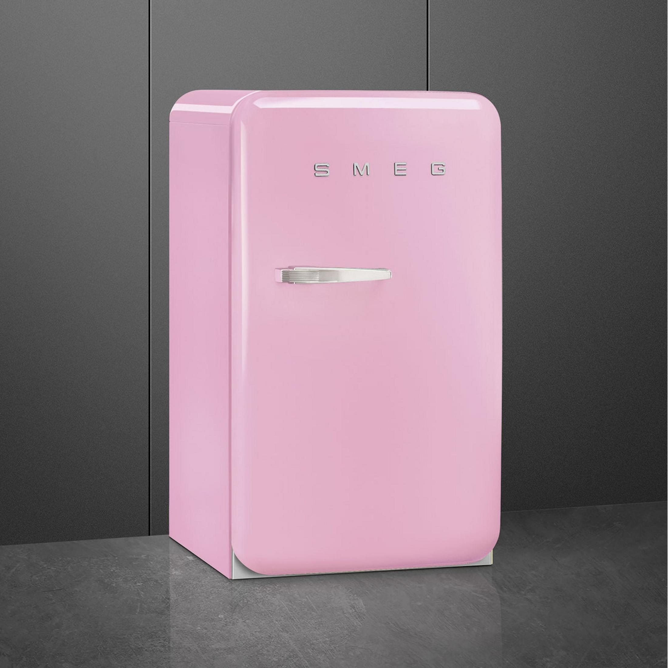 Un refrigerador Smeg rosa con asa plateada sobre suelo oscuro.