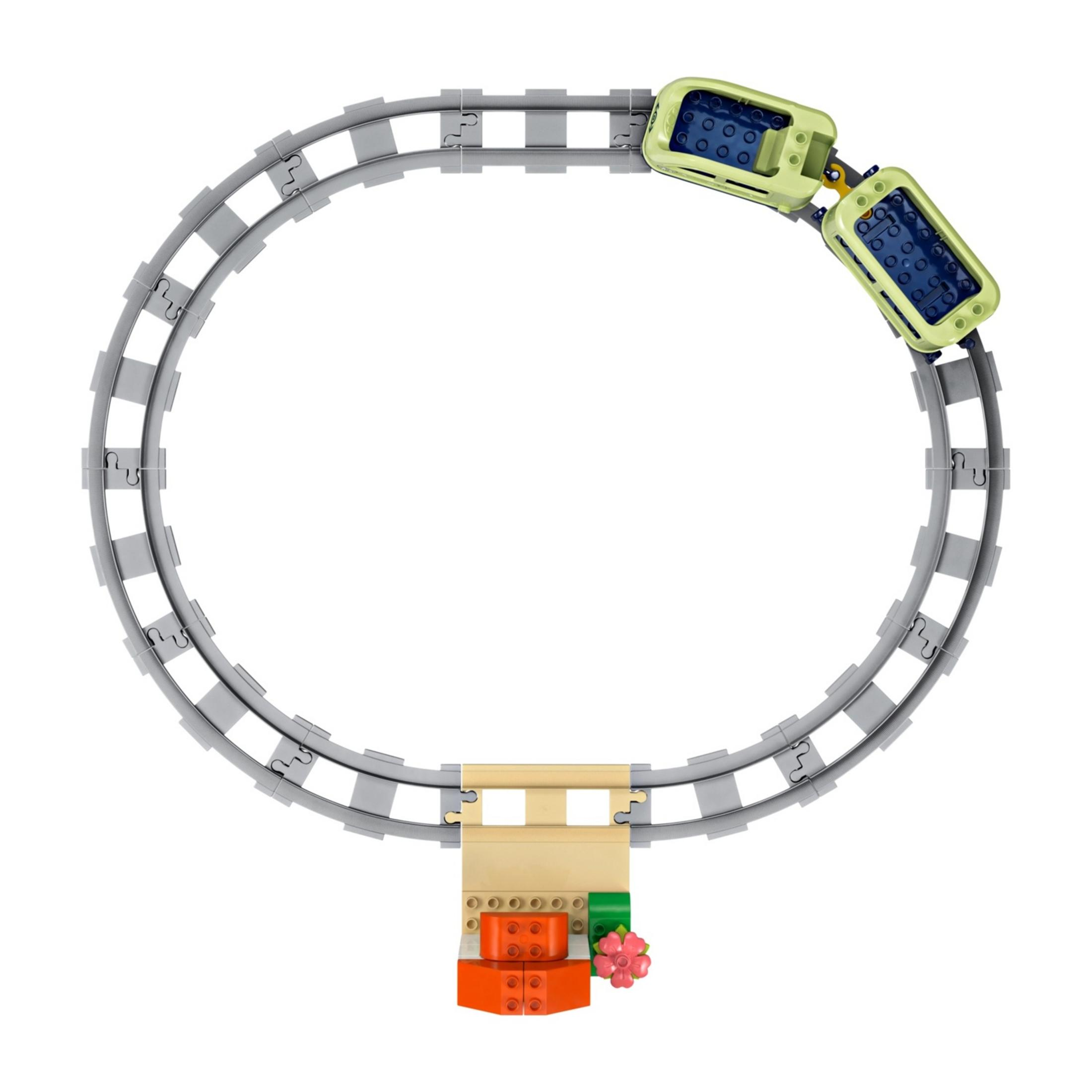 Zabawkowy pociąg z jasnozielonymi wagonami na szarym torze kołowym z kwiatami.