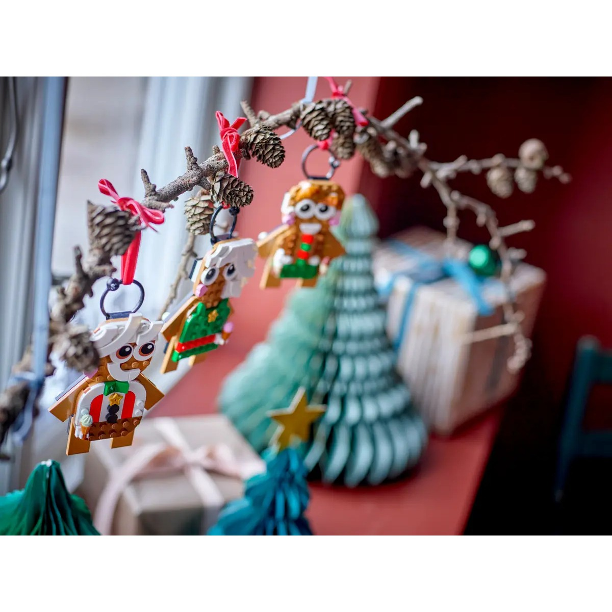 Lego-Weihnachtsfiguren hängen an Zweigen mit Tannenzapfen über Geschenken.