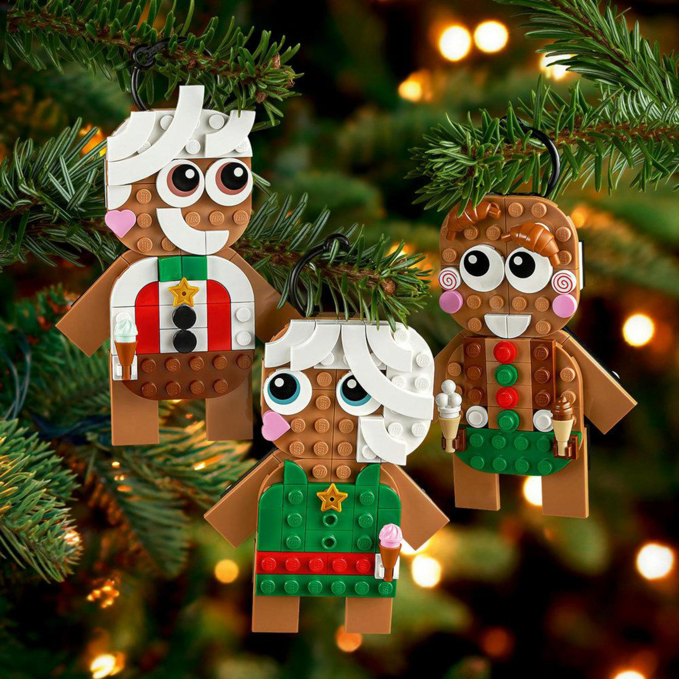 Drei Lego-Lebkuchenfiguren hängen an einem Weihnachtsbaum mit verschwommenen Lichtern.