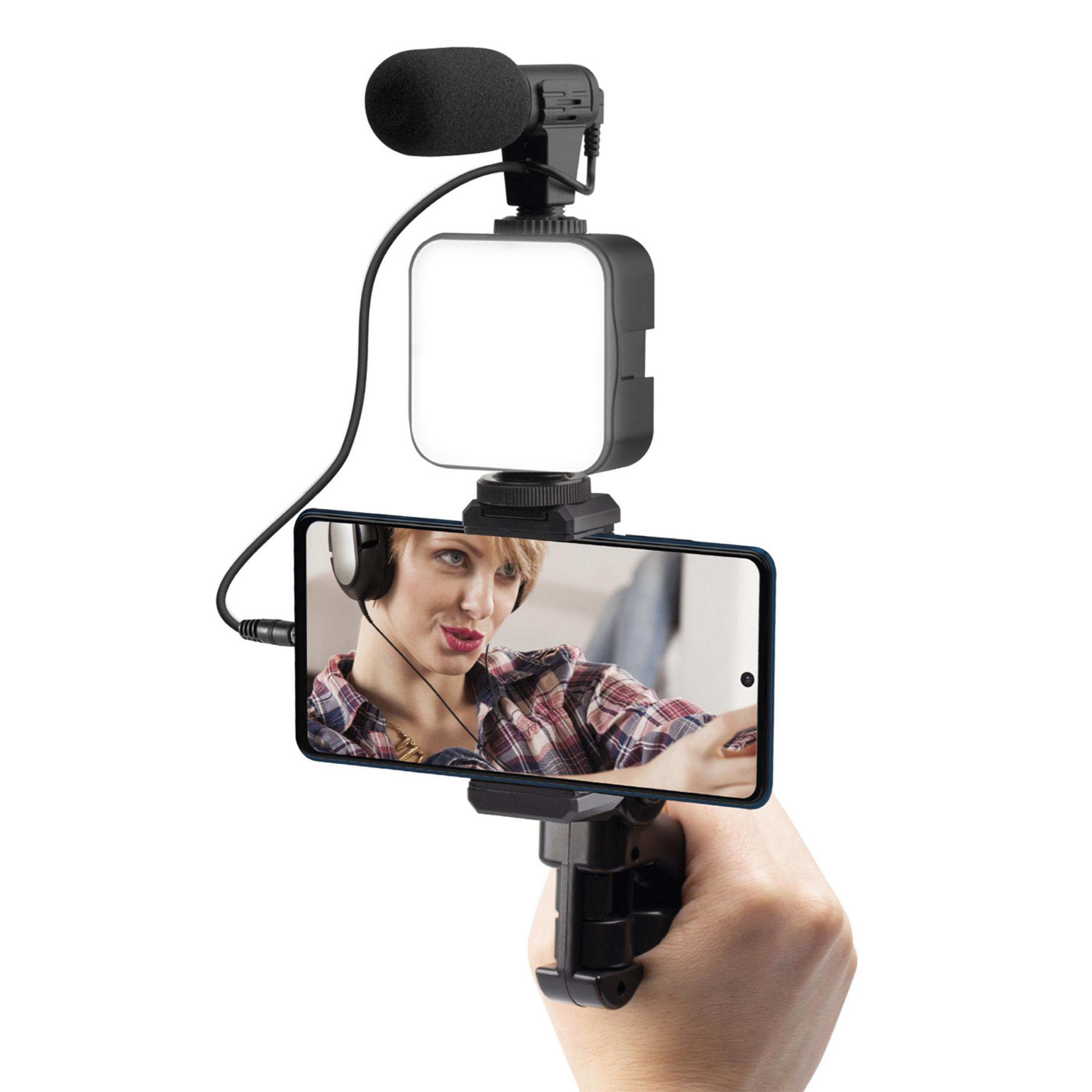 Mano sujetando smartphone con micrófono y luz; mujer en pantalla con auriculares.