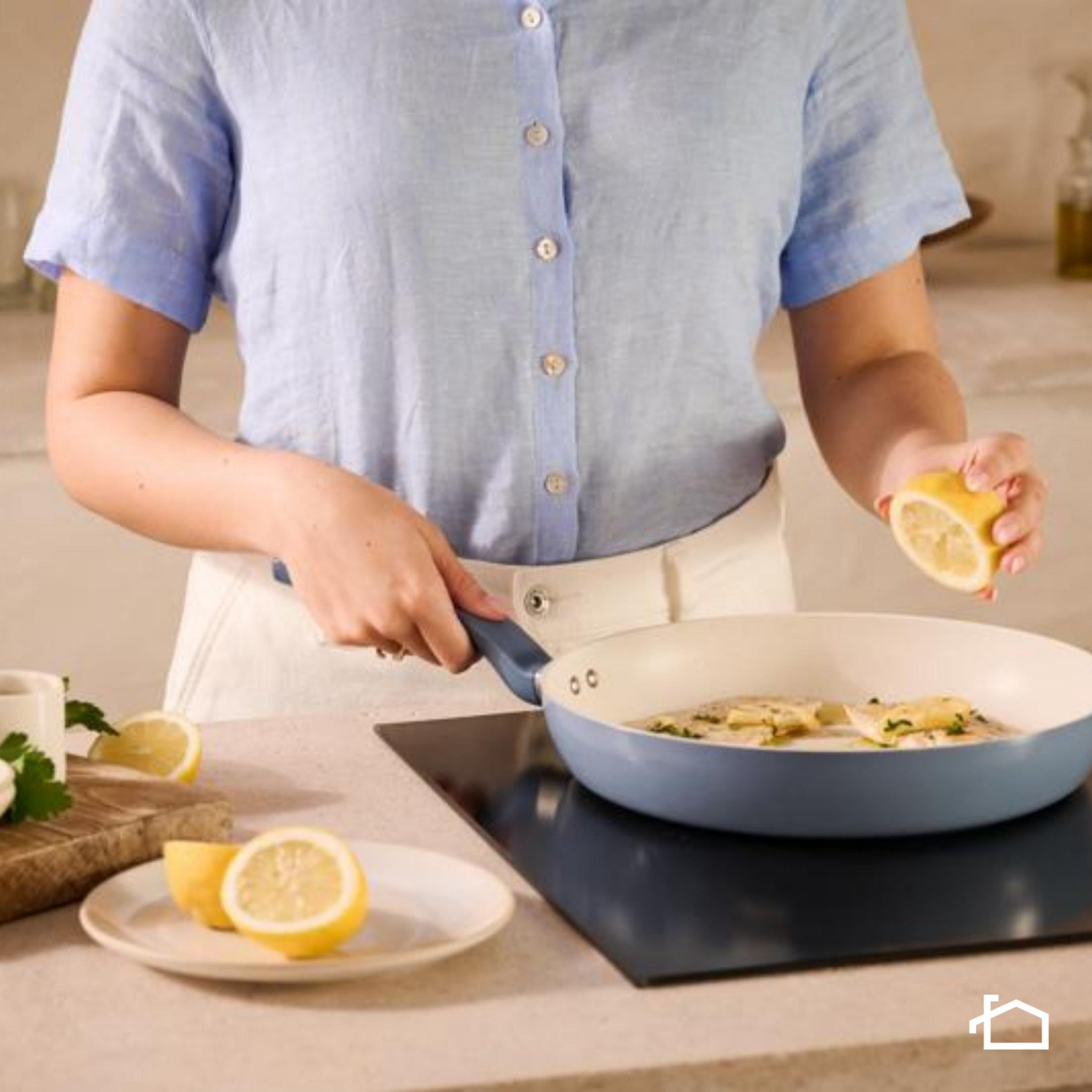 Una persona con una camicia blu spremi un limone su una padella di cibo.