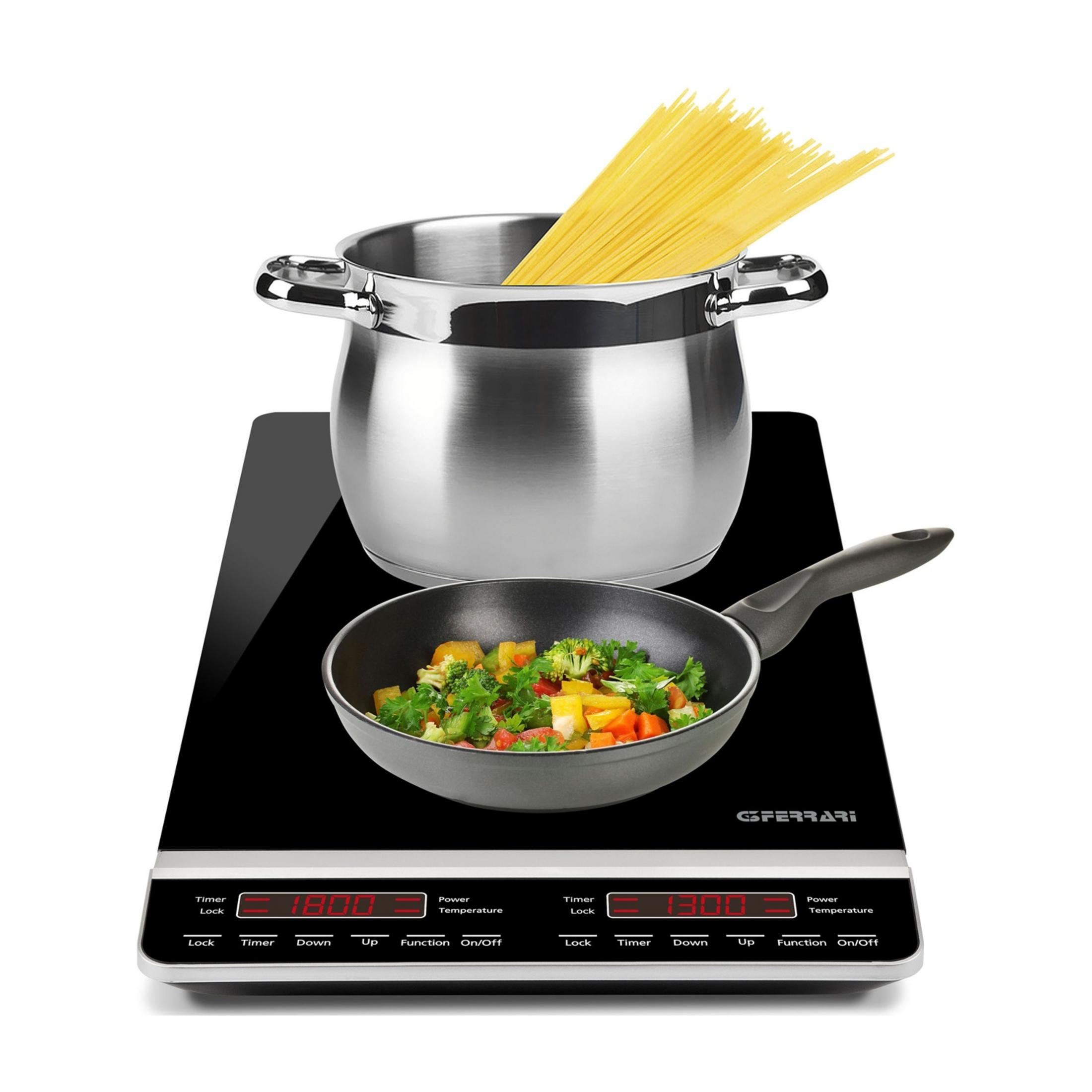 Garnek spaghetti i patelnia z warzywami na płycie indukcyjnej.