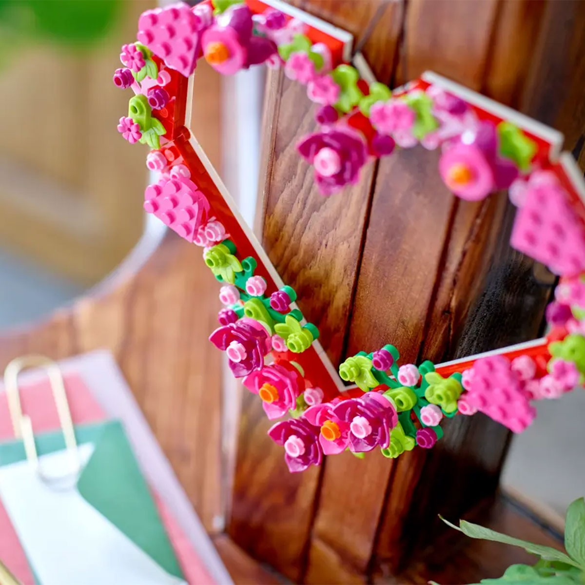 Czerwona ramka w kształcie serca ozdobiona różowymi i zielonymi kwiatami Lego.