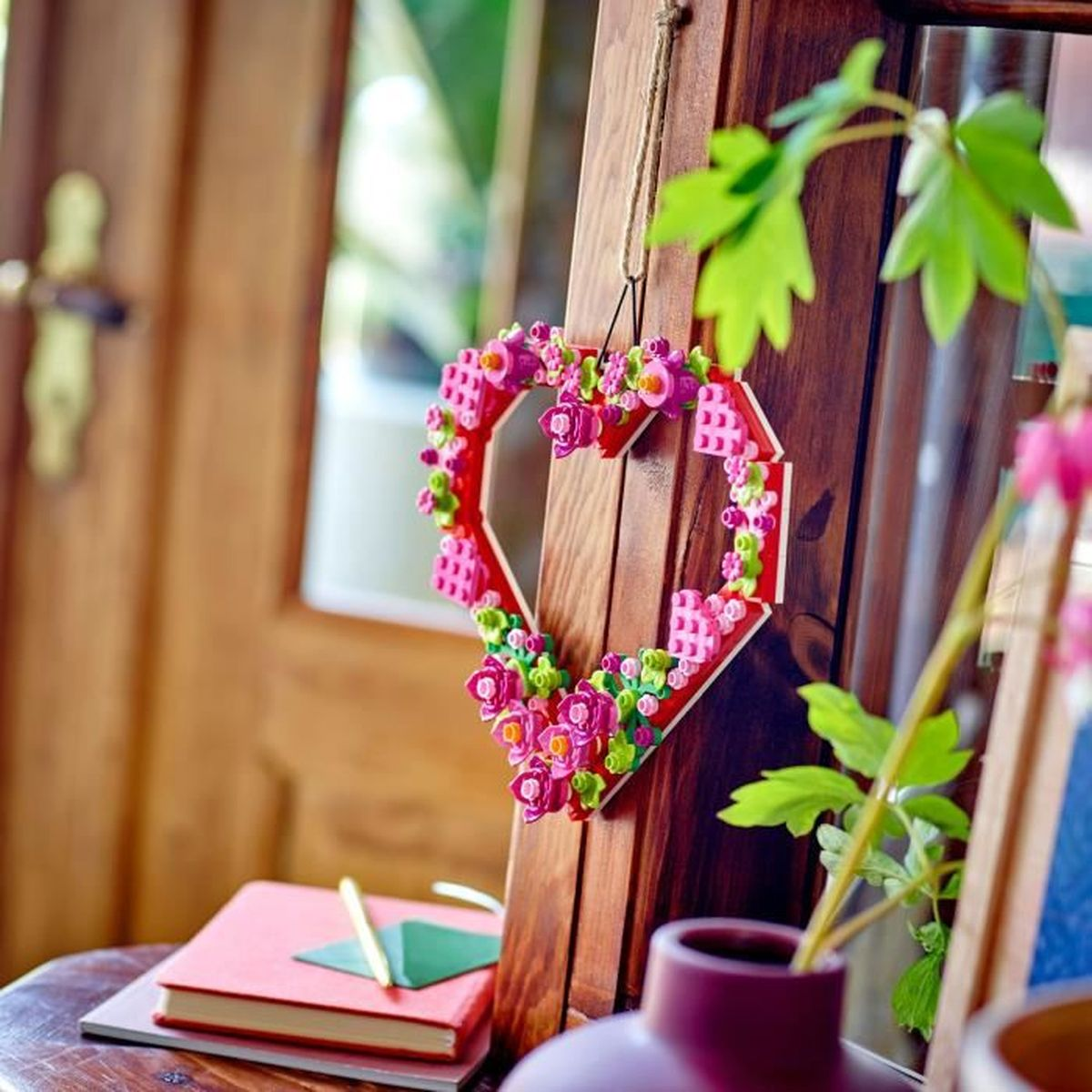 Serce z kolorowych kwiatów Lego wisi na drewnianych drzwiach.