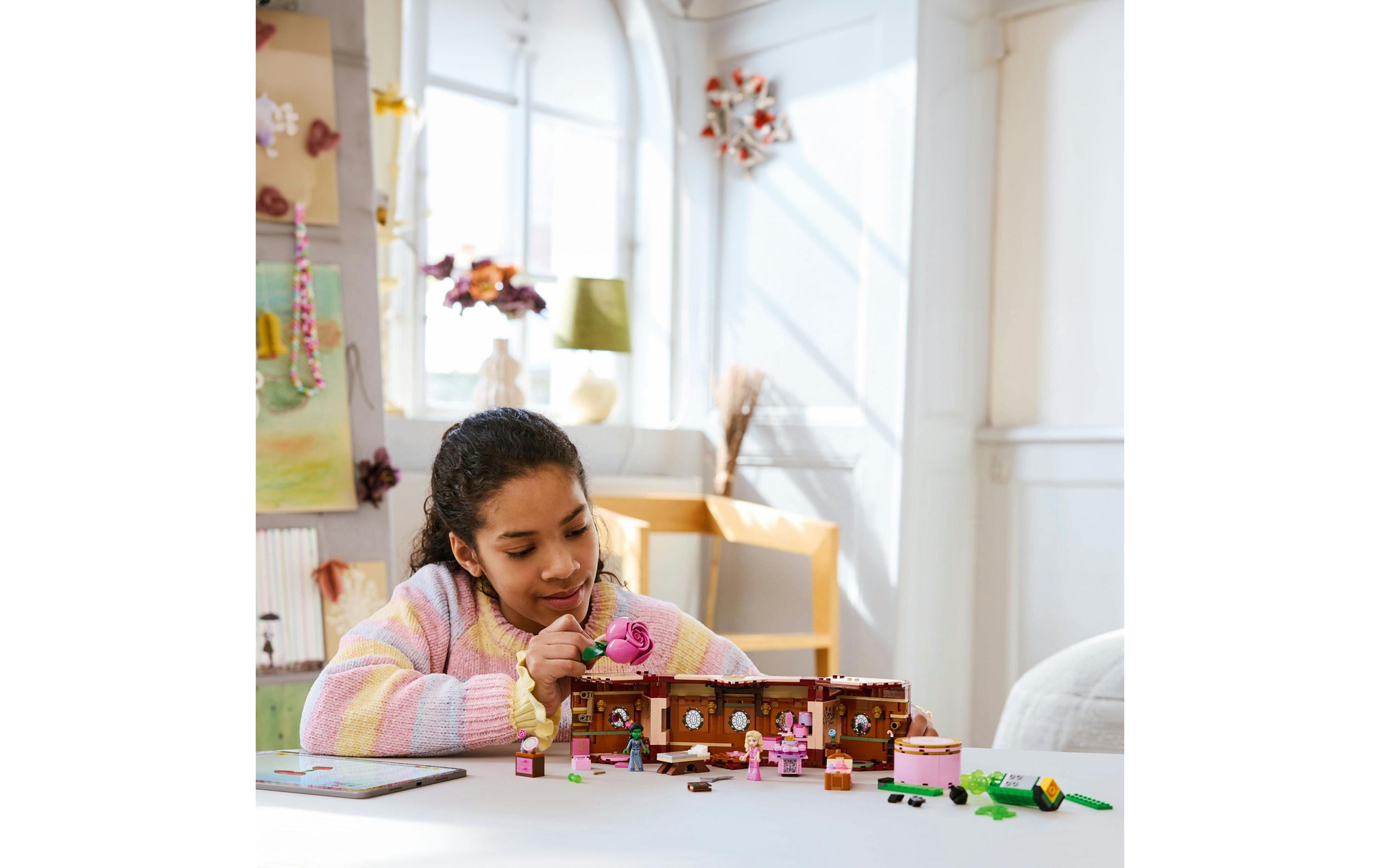 Dziewczynka buduje domek Lego z różową różą, bawi się przy stole.