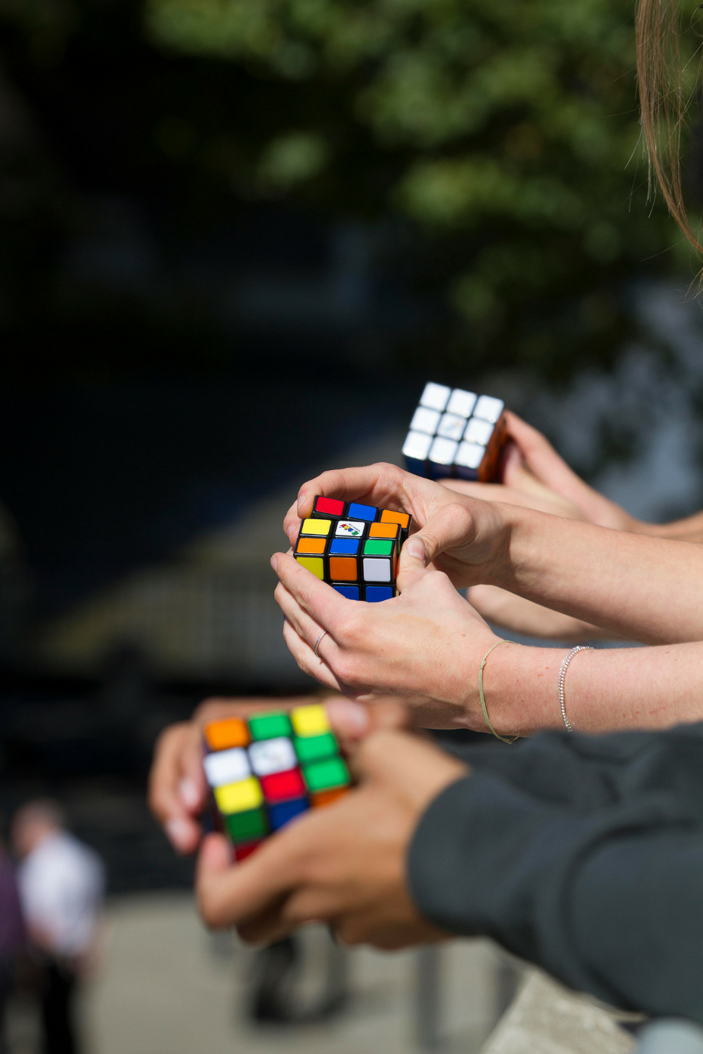 Tres manos sostienen cubos de Rubik con caras coloridas.