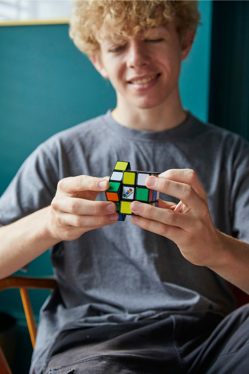 Un chico de pelo rizado sostiene un cubo de Rubik y sonríe.