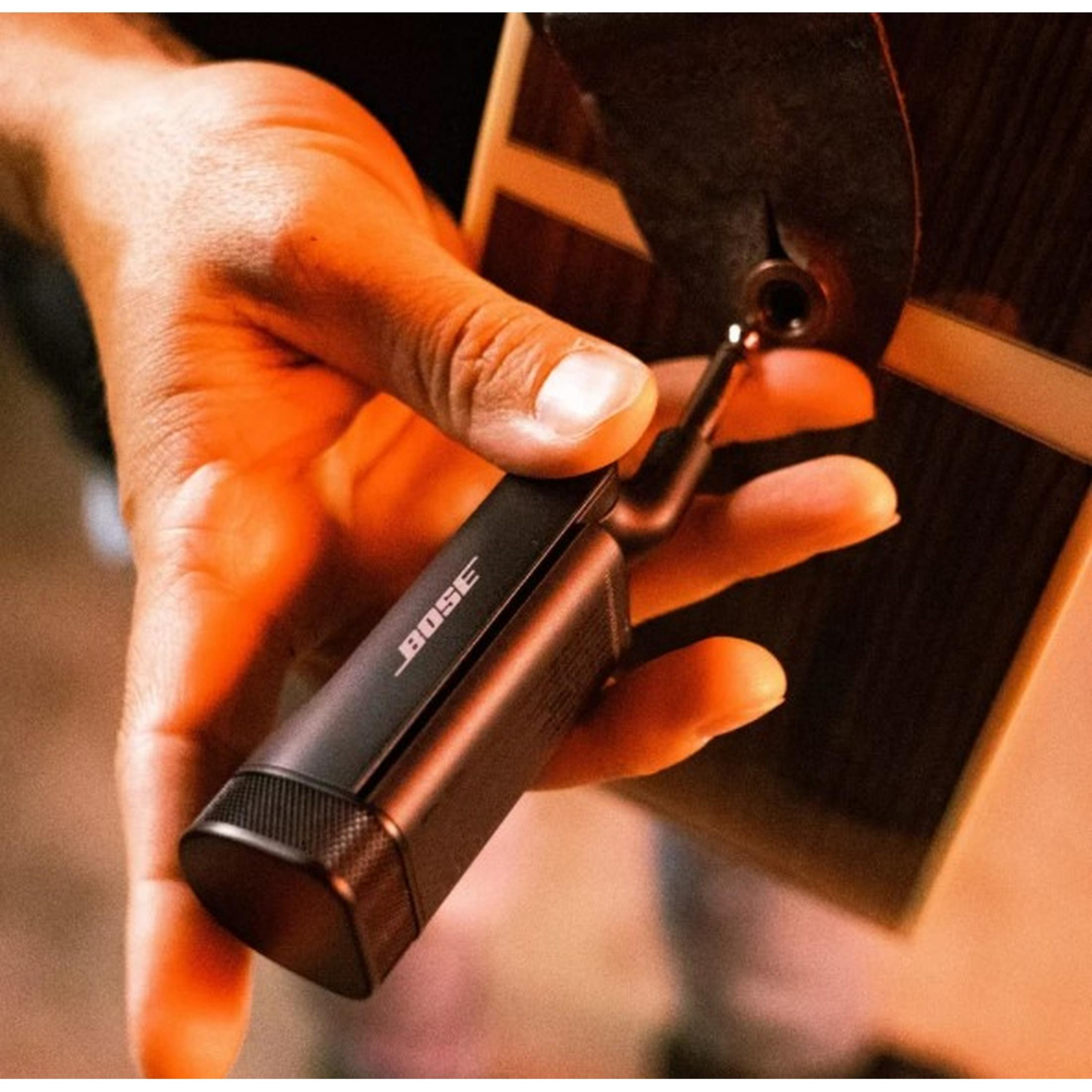 Una mano tiene un dispositivo Bose nero collegato a una chitarra.