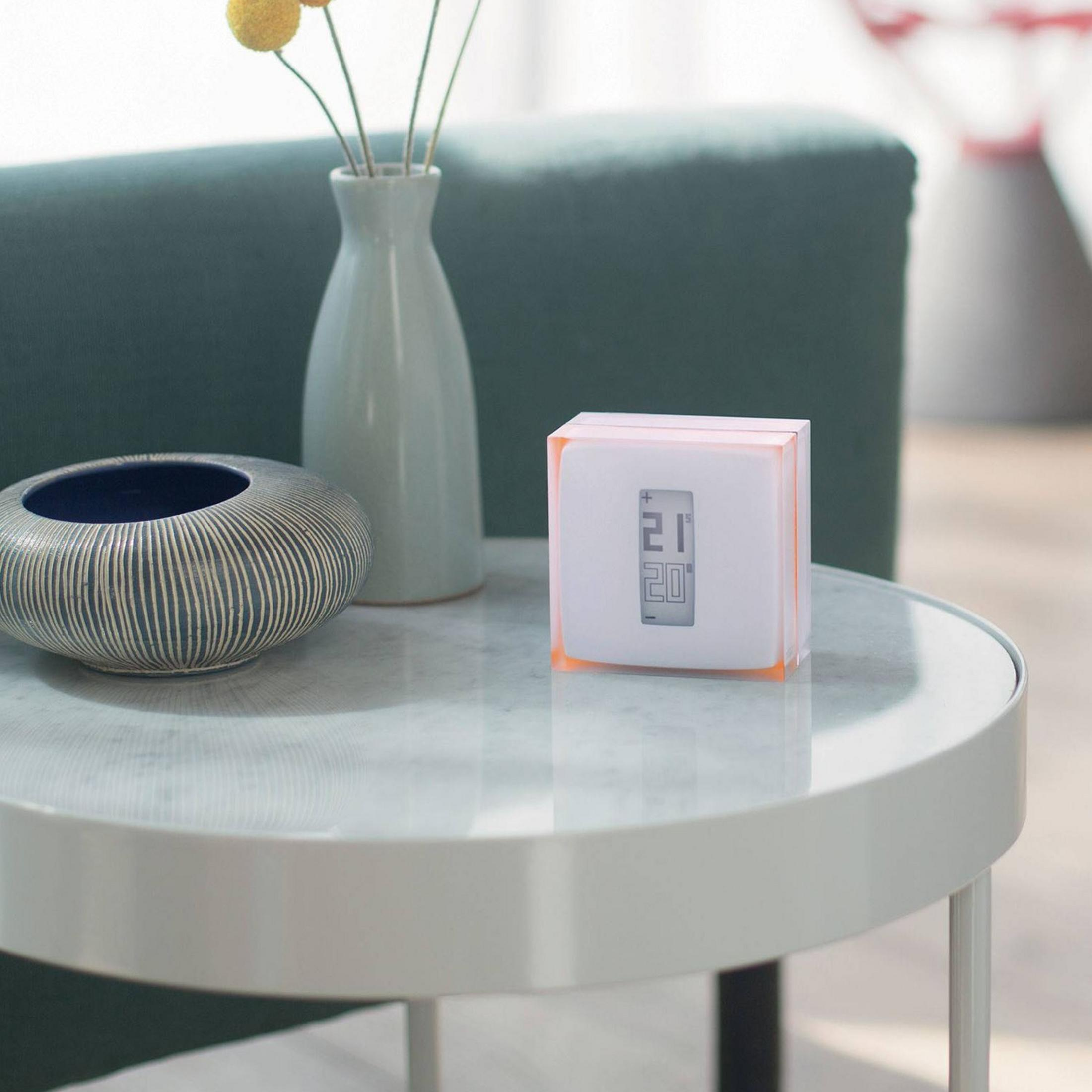 Cyfrowy termostat pokazuje 21 stopni na okrągłym stole z dekoracjami.