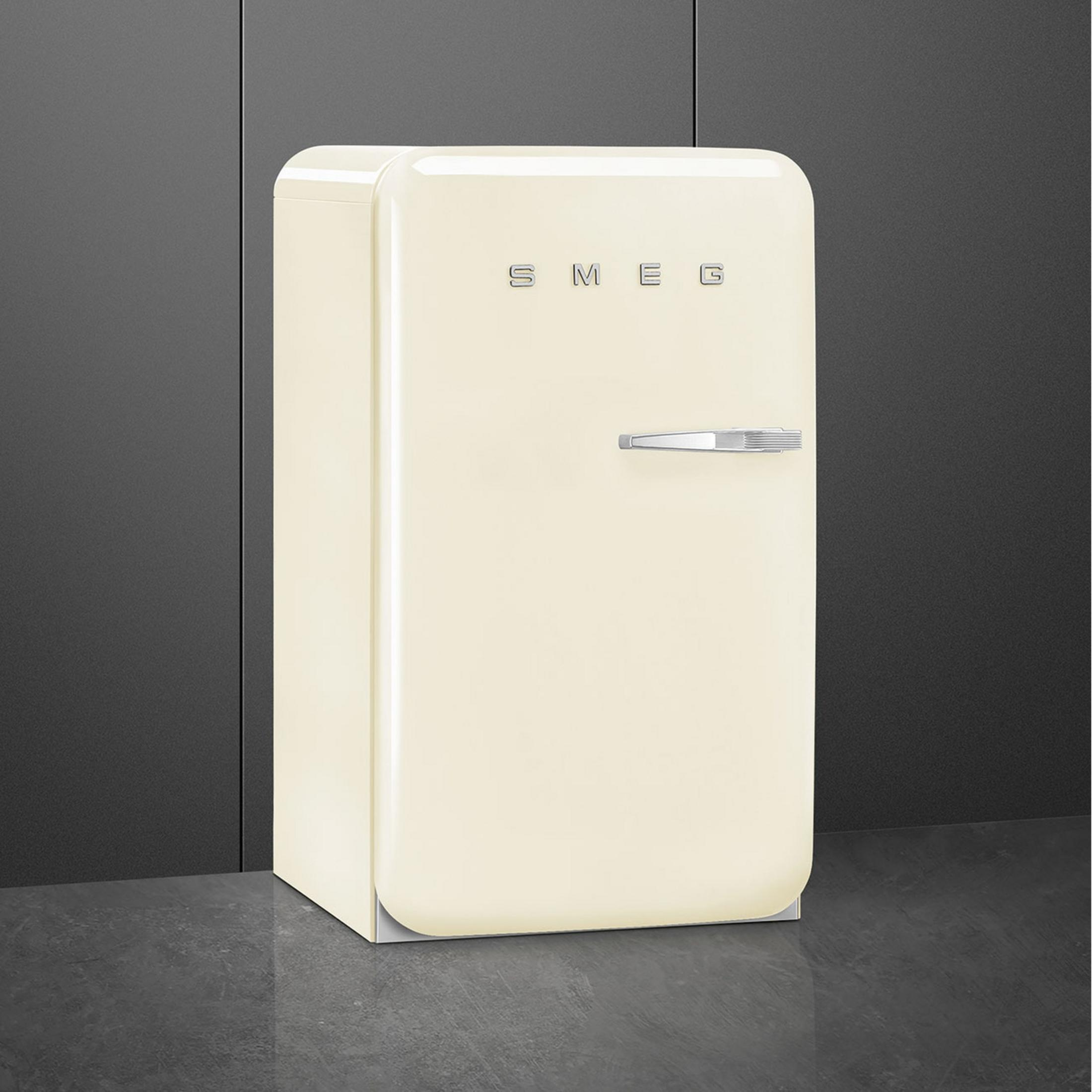 Un refrigerador SMEG color crema sobre suelo oscuro y pared gris.