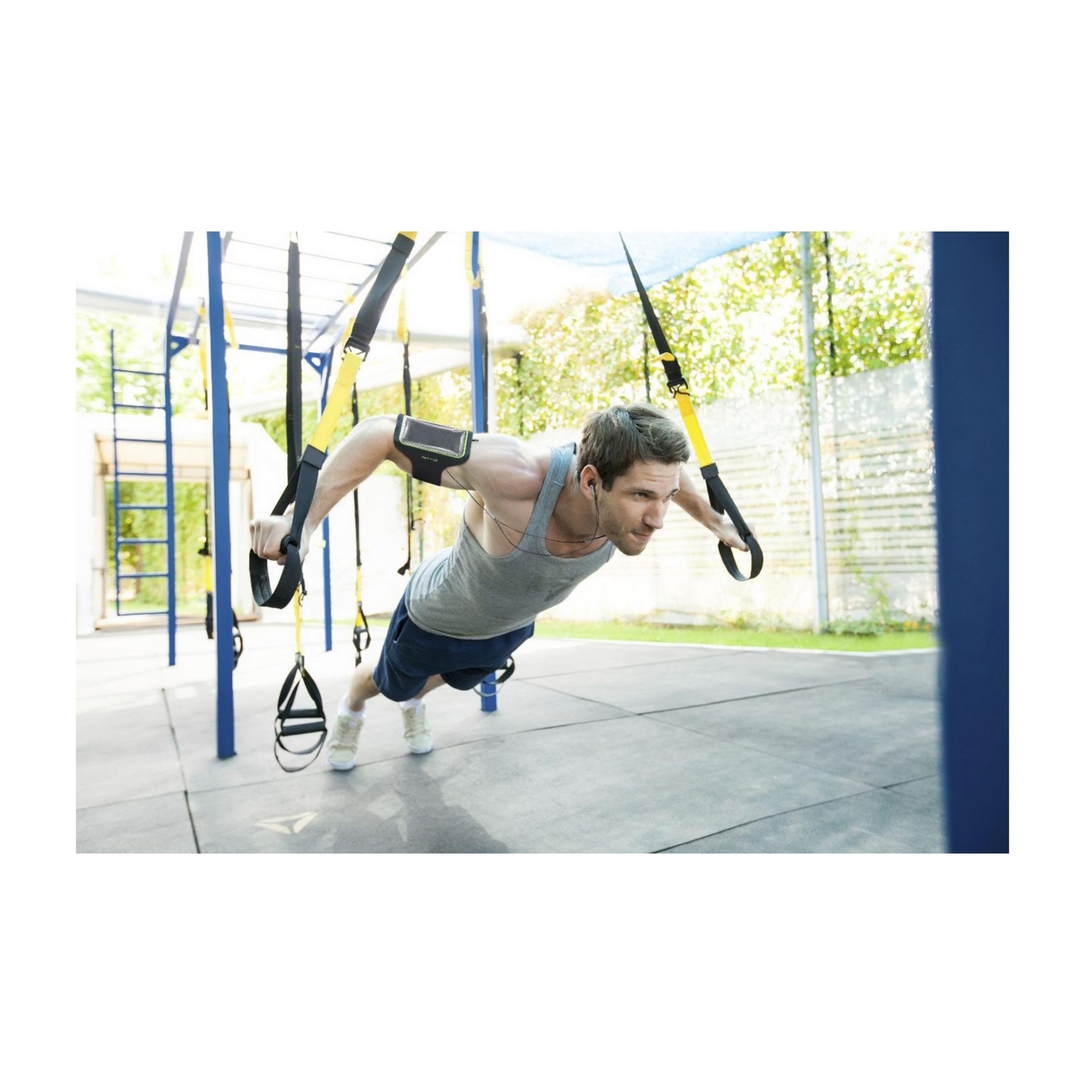 Uomo fa allenamento TRX all'aperto, con fascia da braccio per cellulare.