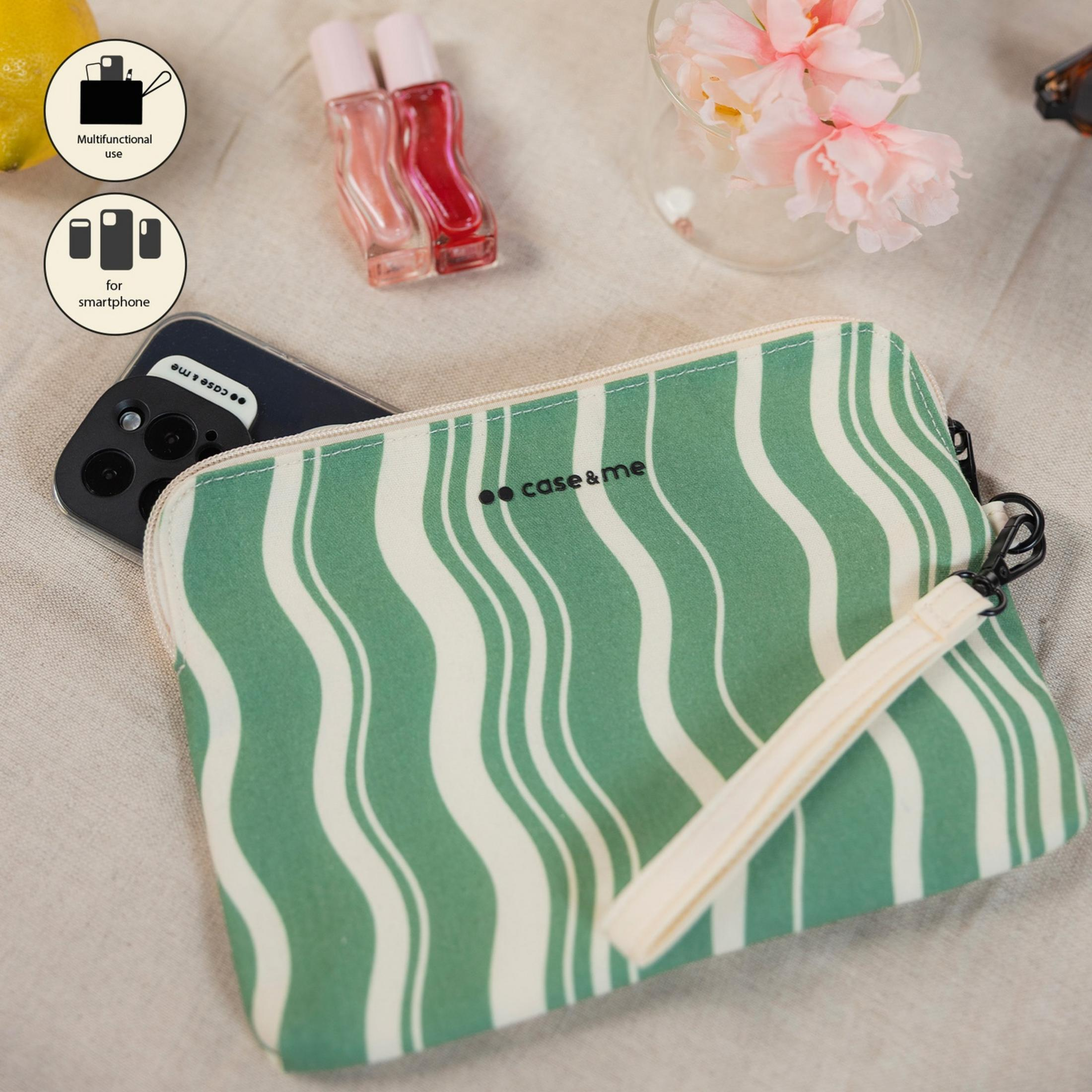 Bolsa verde a rayas con smartphone y botellas de perfume sobre fondo claro.