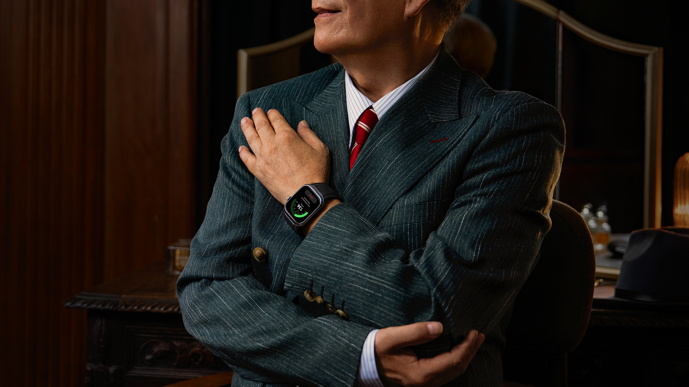Mężczyzna w garniturze w prążki z czerwoną krawatką patrzy na ekran smartwatcha.