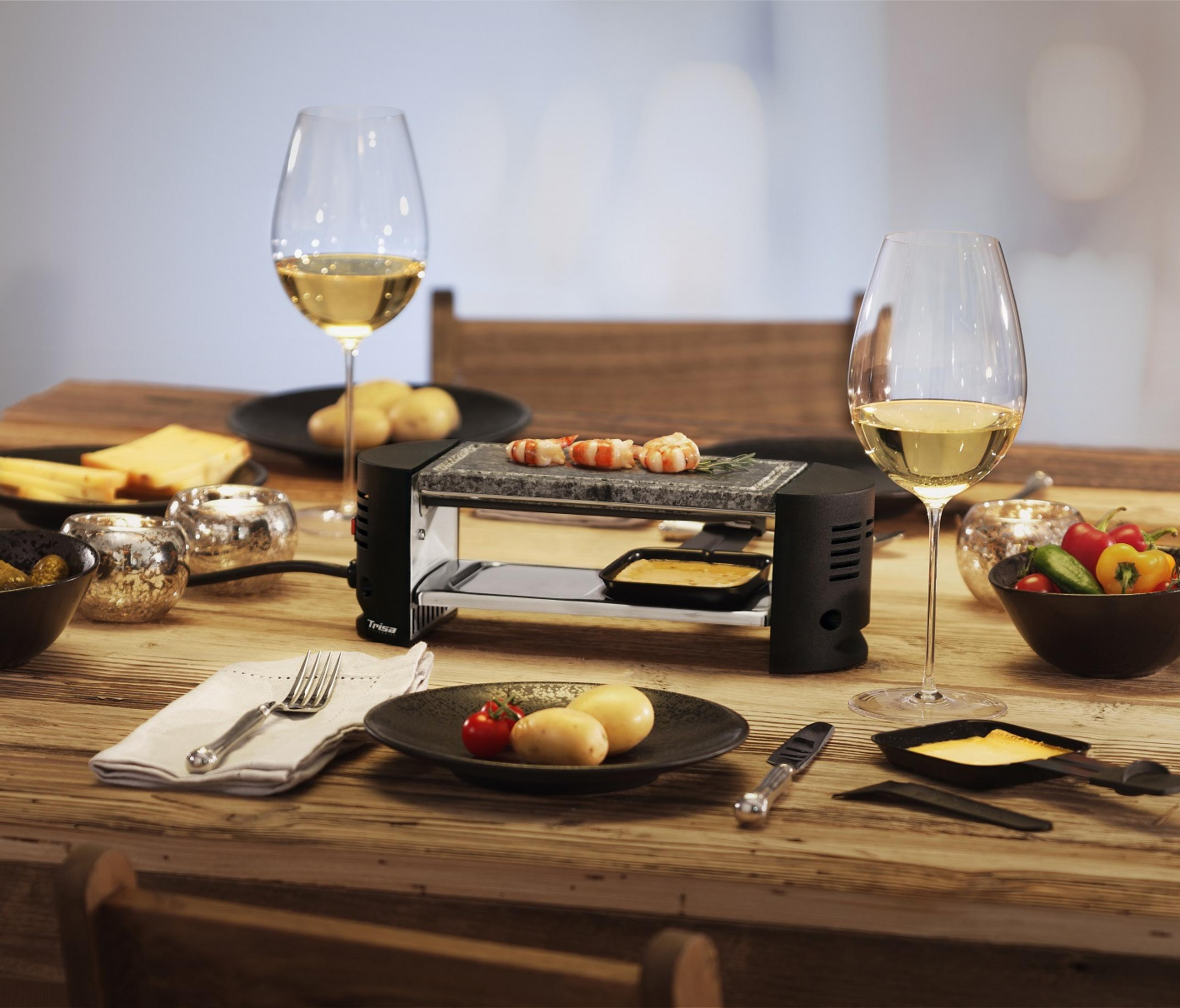 Raclette-Grill mit Garnelen, Kartoffeln, Käse und Wein auf einem Holztisch.