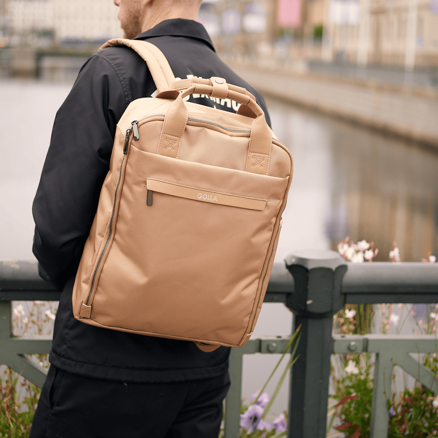 Mann mit hellbraunem Rucksack über der Schulter, Blick über Wasser.