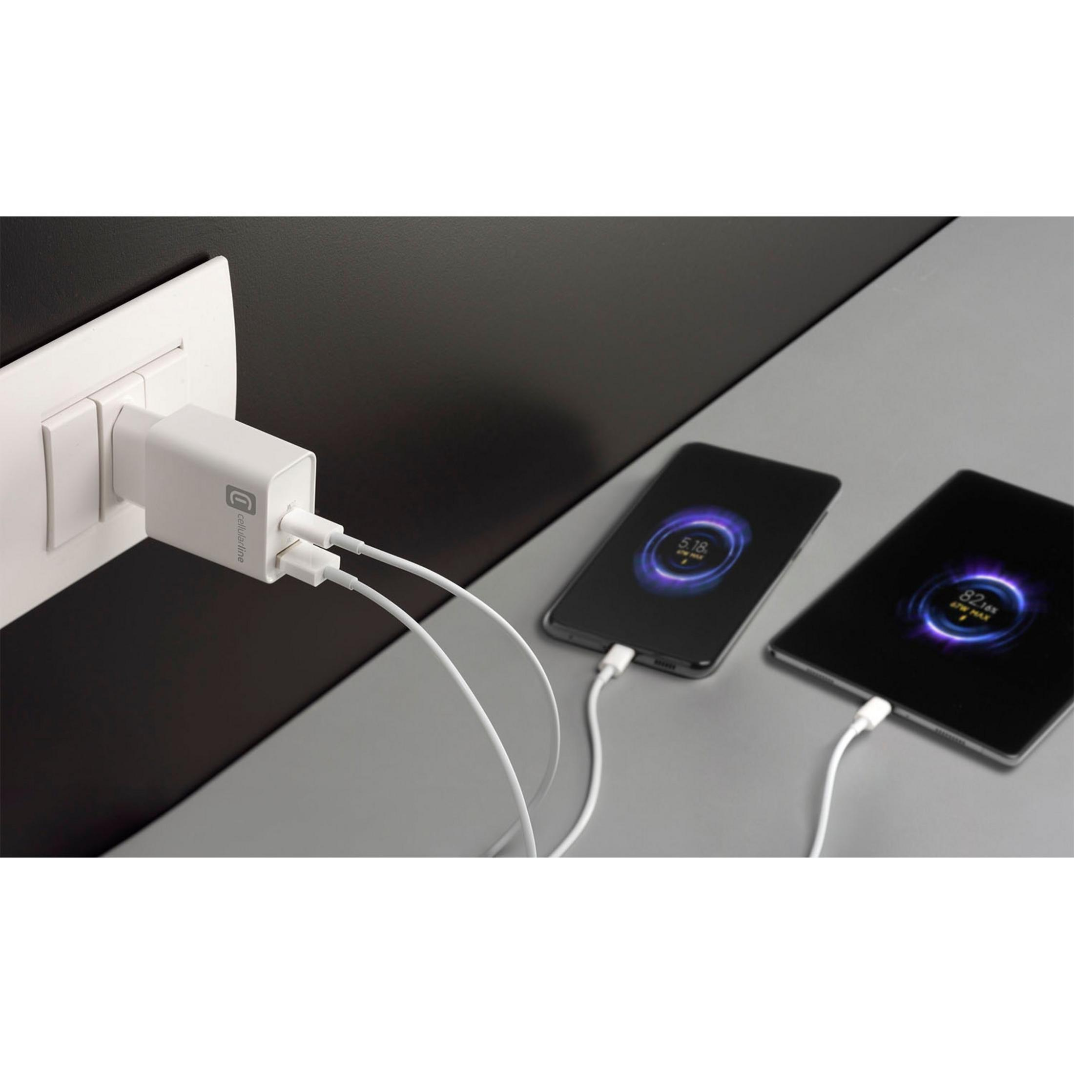 Un adaptador de carga blanco enchufado a un enchufe, cargando dos teléfonos.