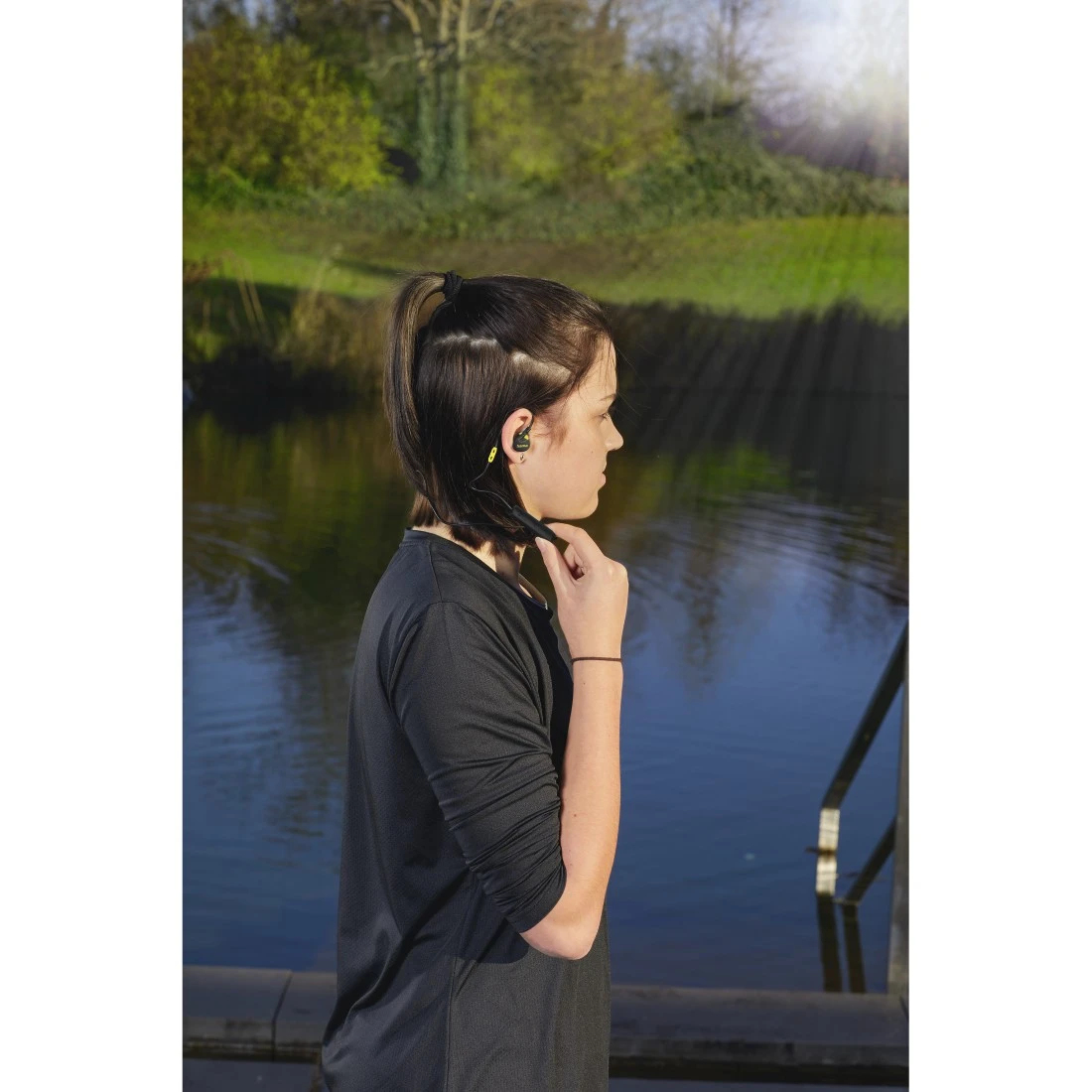 Kobieta z kucykiem i słuchawkami stoi nad wodą.