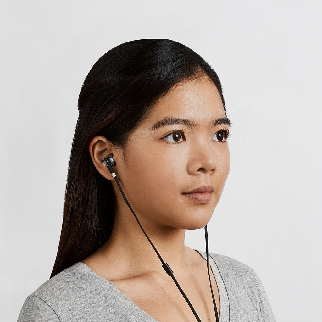 Una giovane donna con lunghi capelli scuri indossa auricolari.