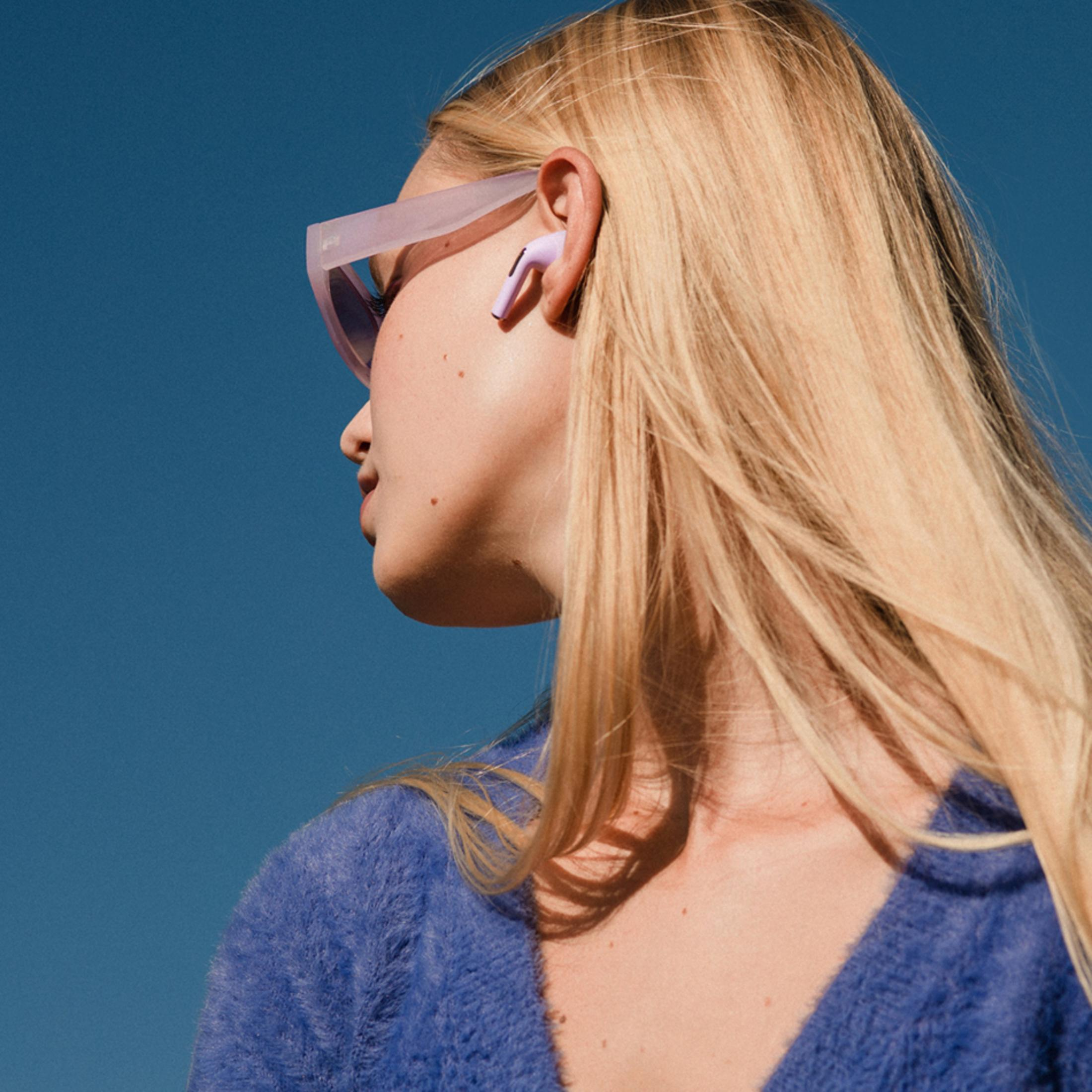 Una donna dai capelli biondi indossa auricolari viola e un maglione blu.