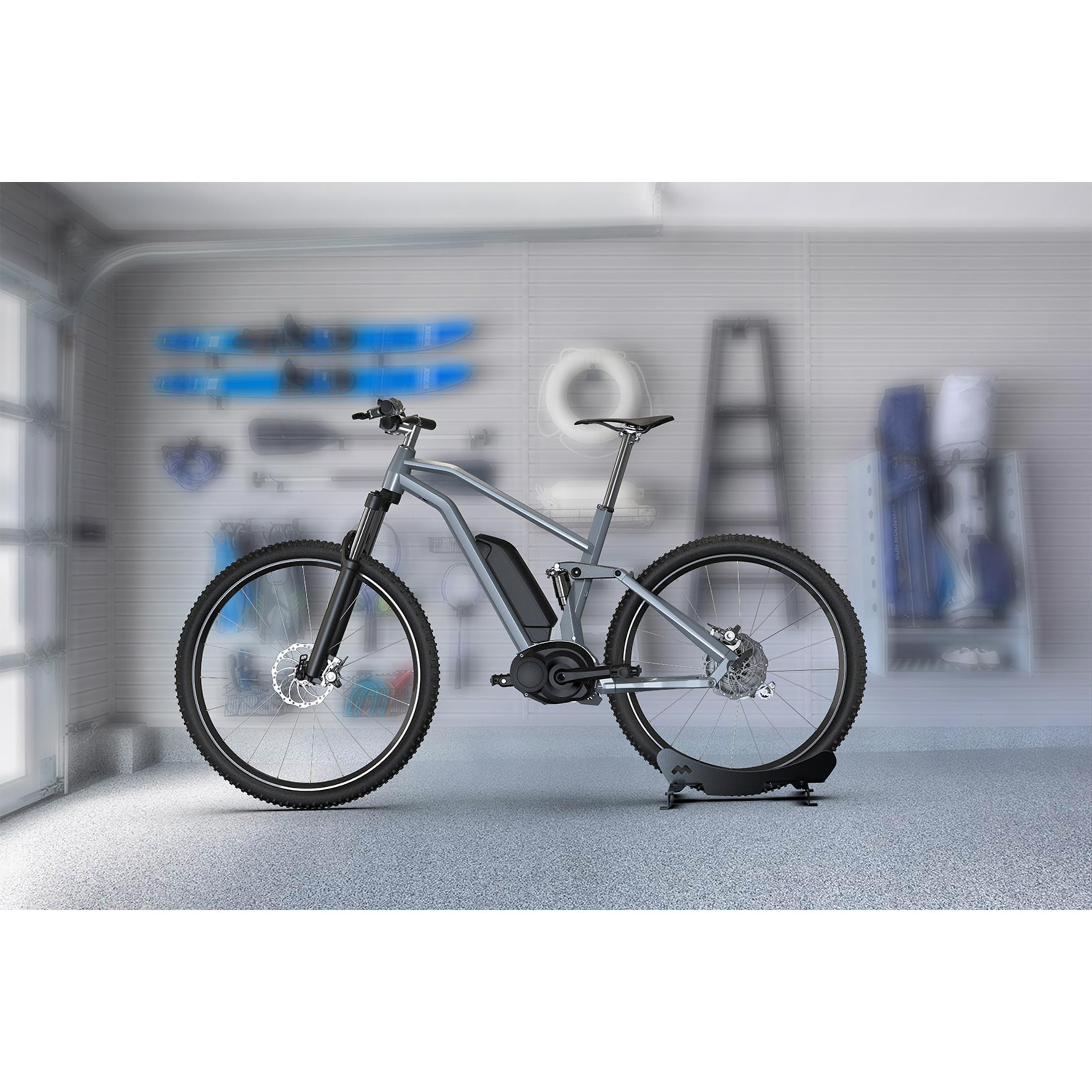 Szary rower elektryczny w garażu z narzędziami i sprzętem na ścianie.