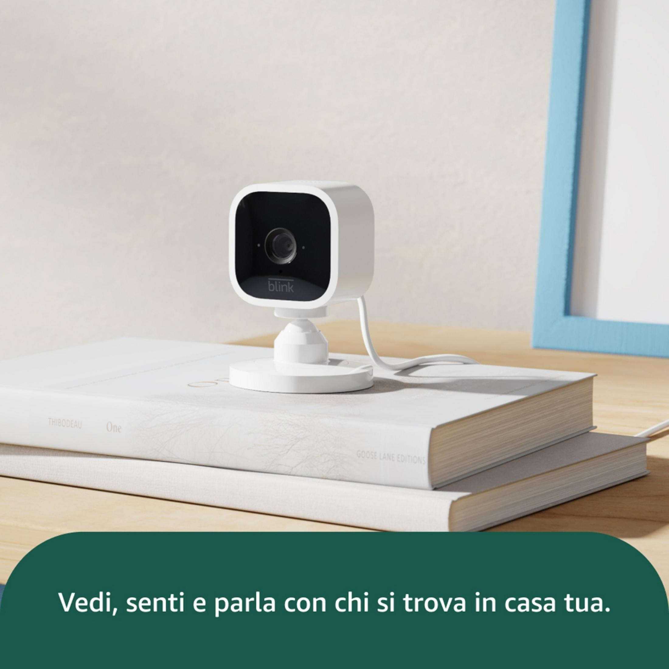 Biała kamera Blink stoi na książce obok niebieskiej ramki na zdjęcie.