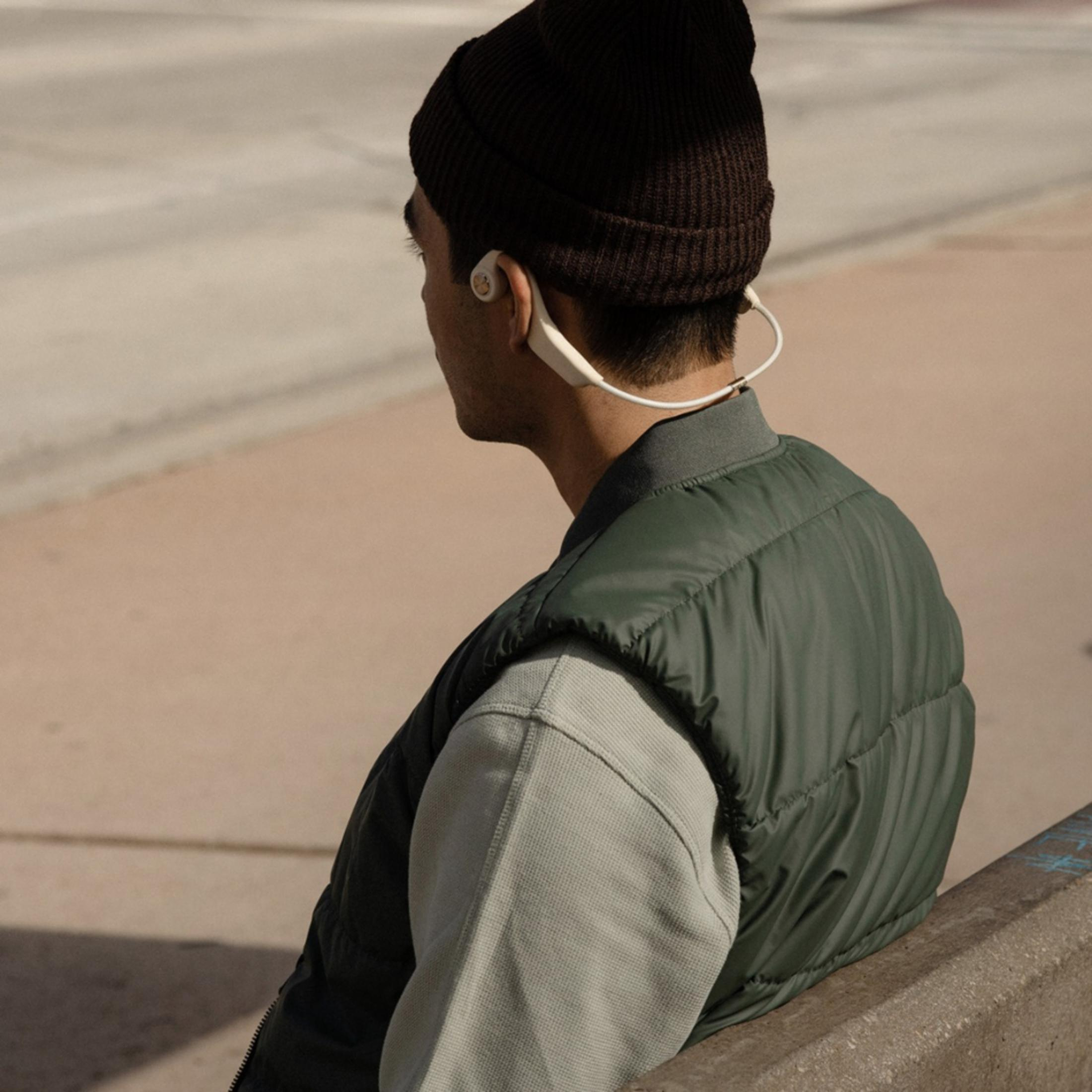 Uomo con berretto marrone e gilet verde indossa auricolari bianchi.