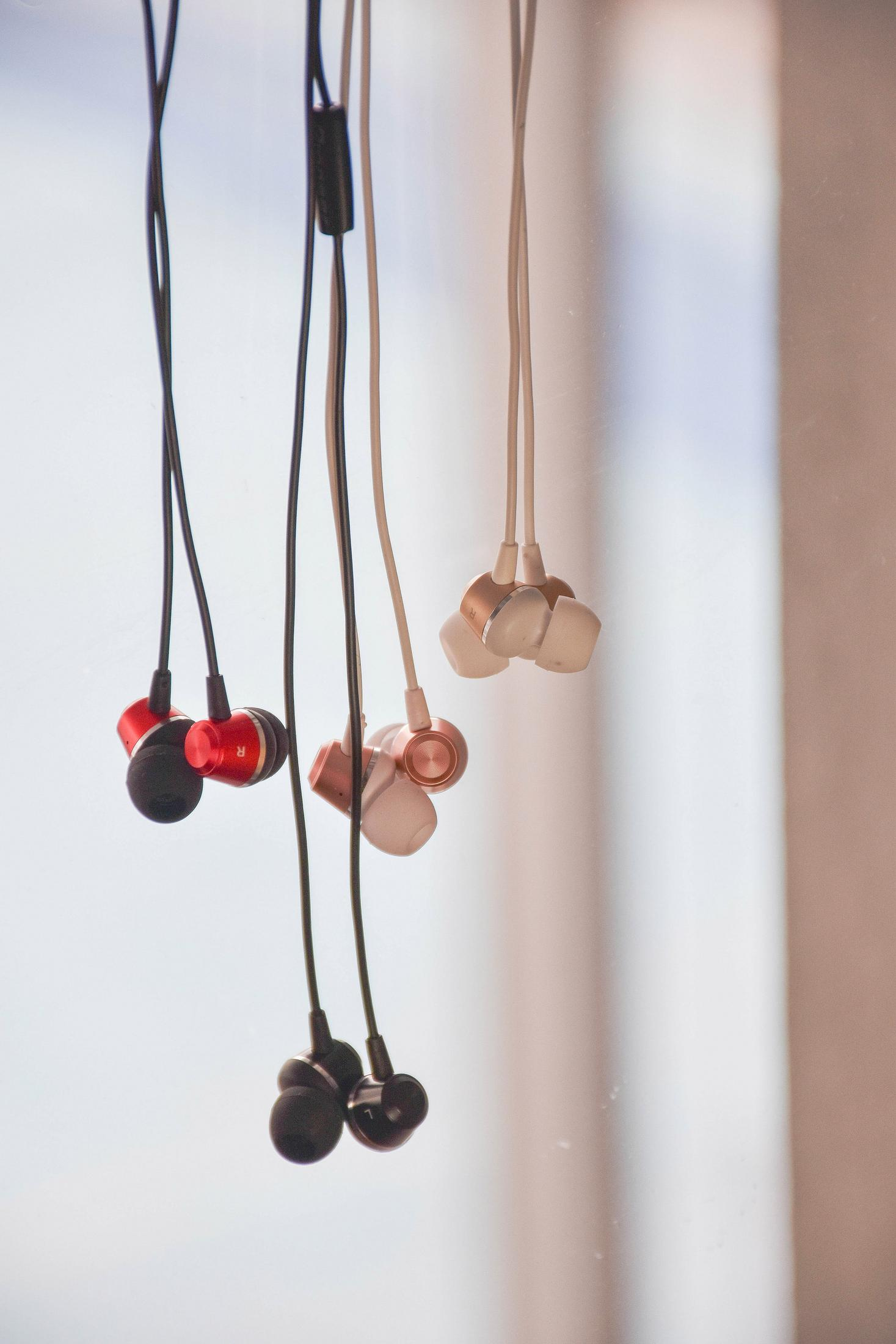 Trzy pary słuchawek: czerwono-czarne, różowo-złote i ciemnoszare wiszą na kablach.